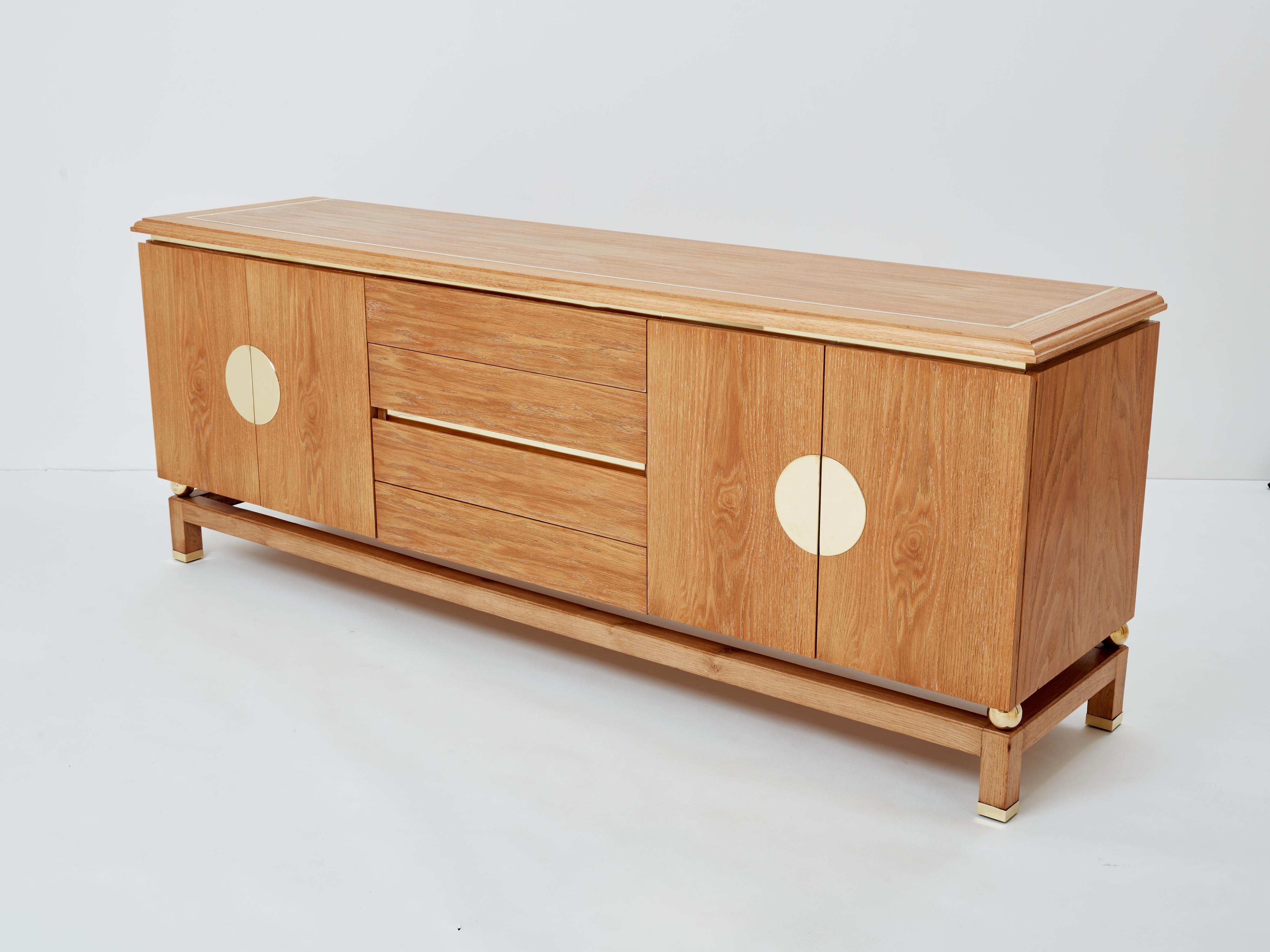 This beautiful cerused oak sideboard was designed by Italian mid-century modern designer Tommaso Barbi in the 1970s. It features four doors and four drawers at its center. Gleaming brass accents, with rounded shape brass inlays on the doors, four
