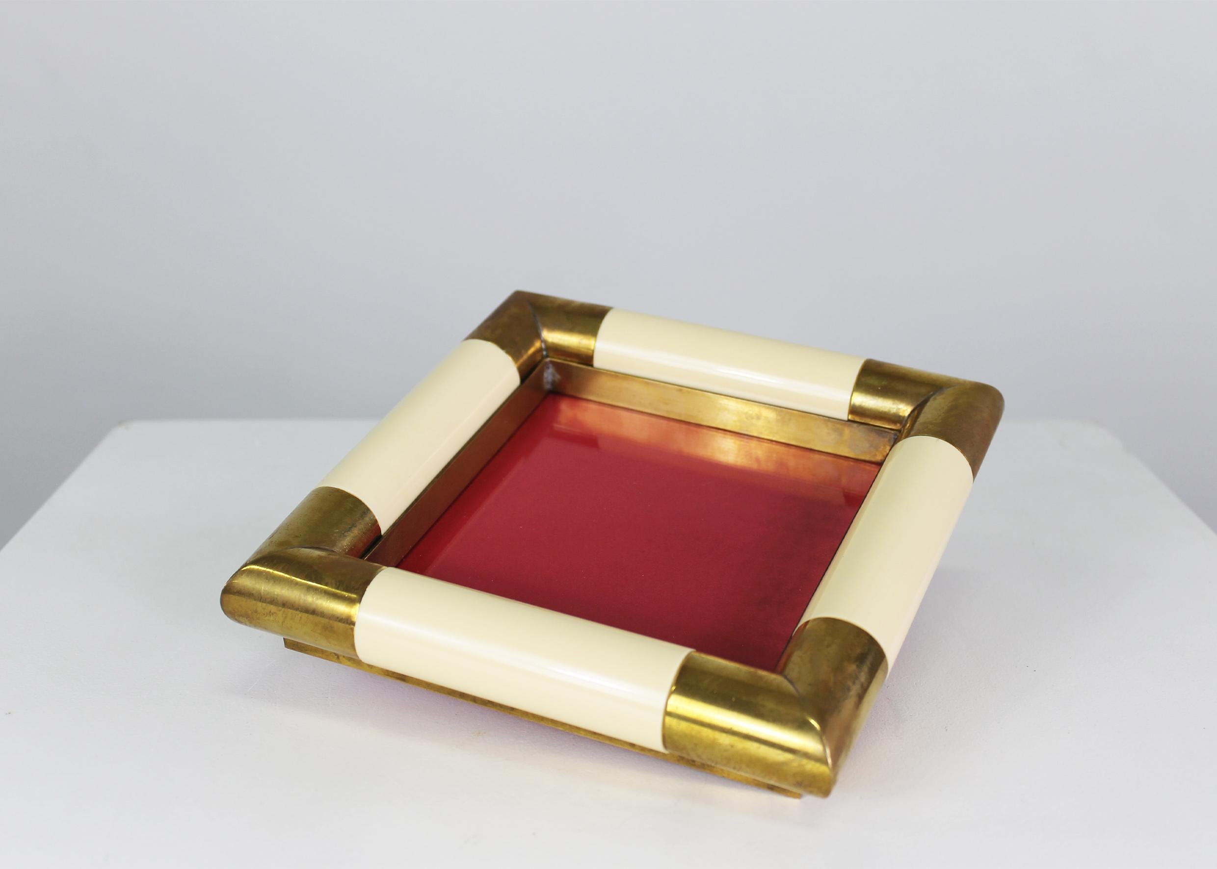 Vide Poche con estructura de latón con inserciones decorativas de resina, la parte central es de cristal y muestra la base inferior recubierta de terciopelo rojo.
Esta pieza decorativa fue diseñada por Tommaso Barbi en la década de 1970. 
