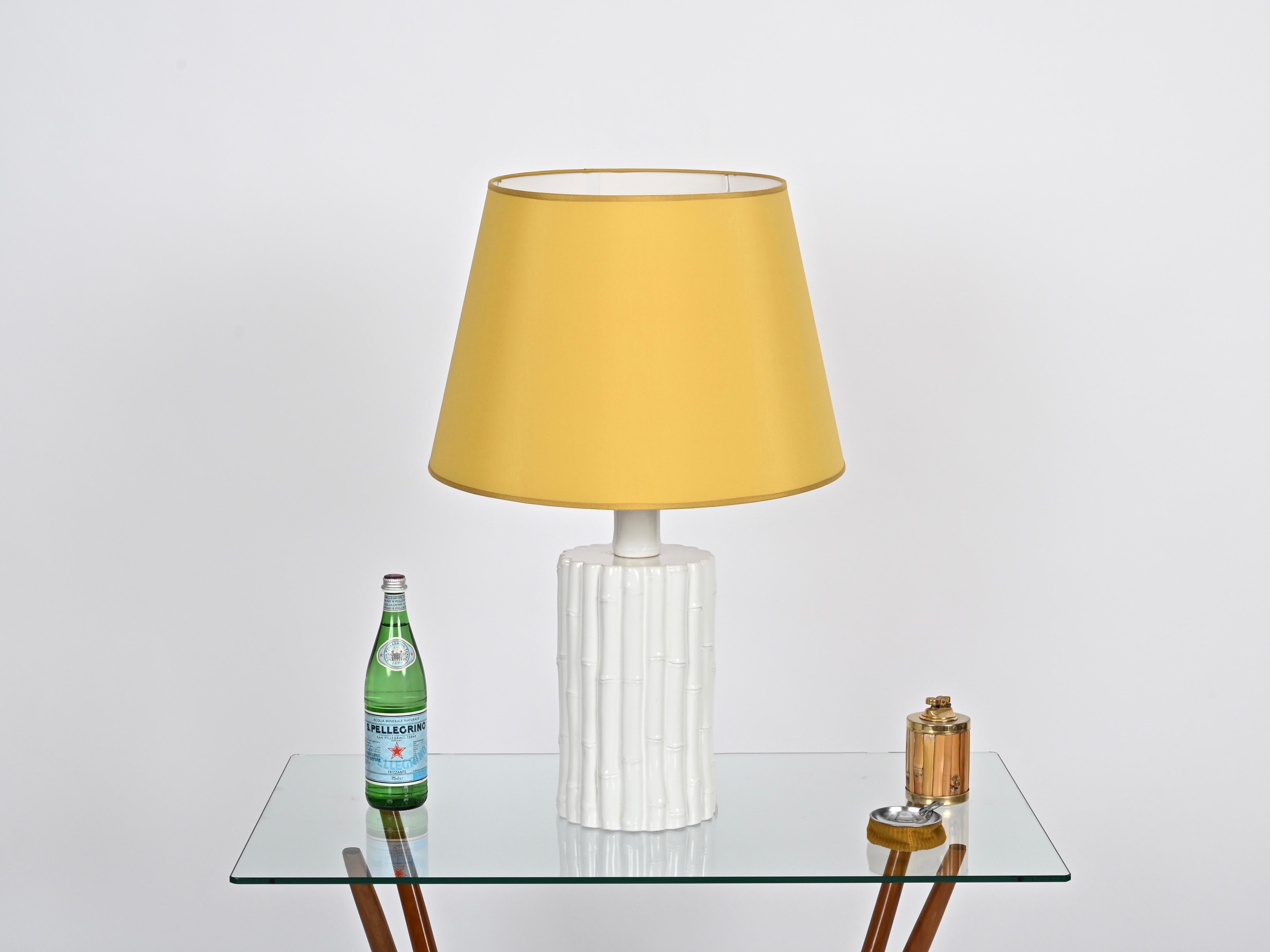 Spectacular midcentury large table lamp in  faux bamboo glazed white ceramic completed by a beautiful yellow toned cotton lampshade. This gorgeous lamp is signed on the bottom by Tommaso Barbi and was produced in Italy during the 1970s.  

This