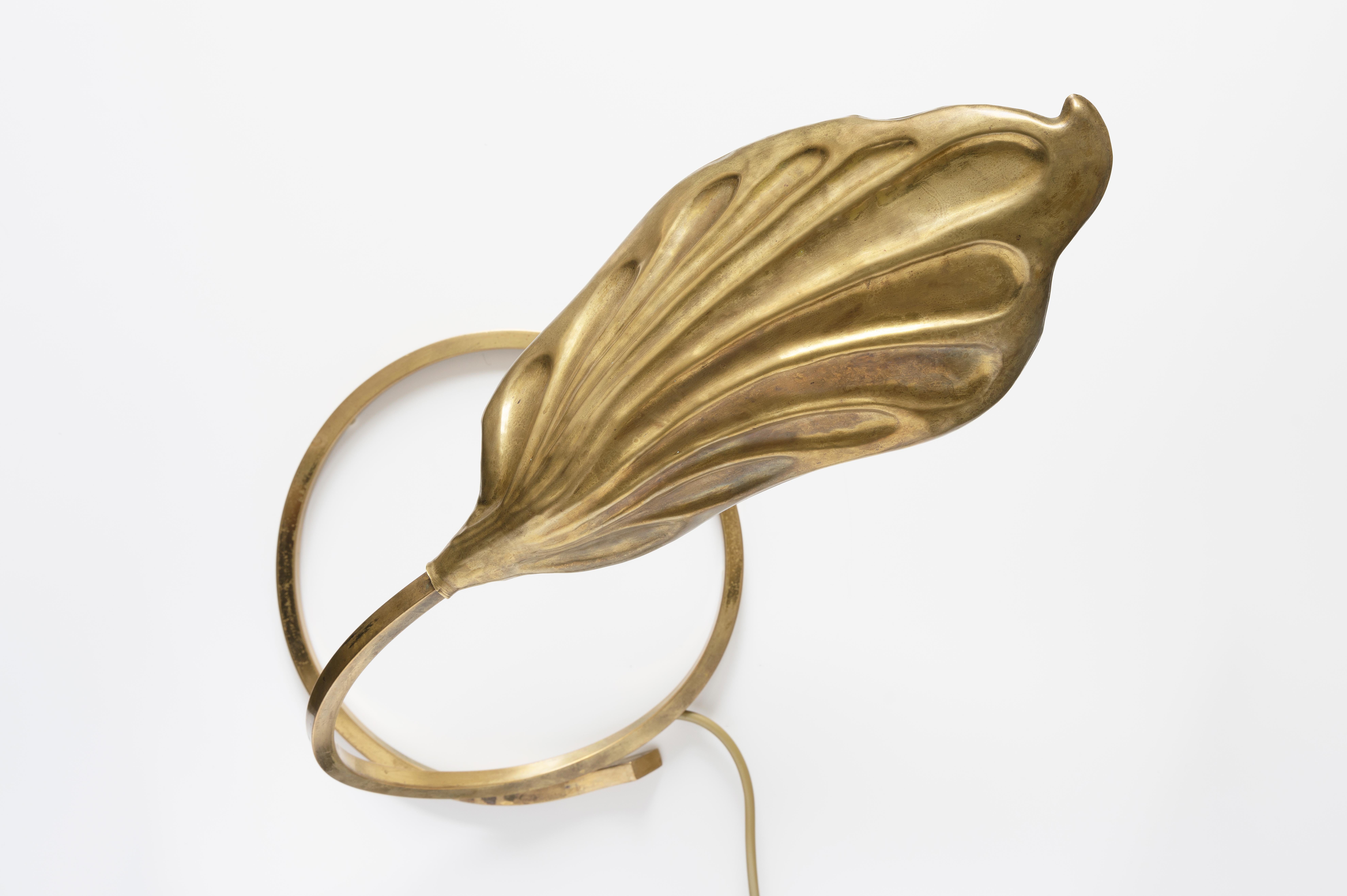 This iconic single leaf table lamp designed by Tommaso Barbi and Carlo Giorgi was produced by Bottega Gadda in Italy in the 1970s. The circular brass frame sweeps upwards from the base to support the large, decorative, hammered brass leaf. The