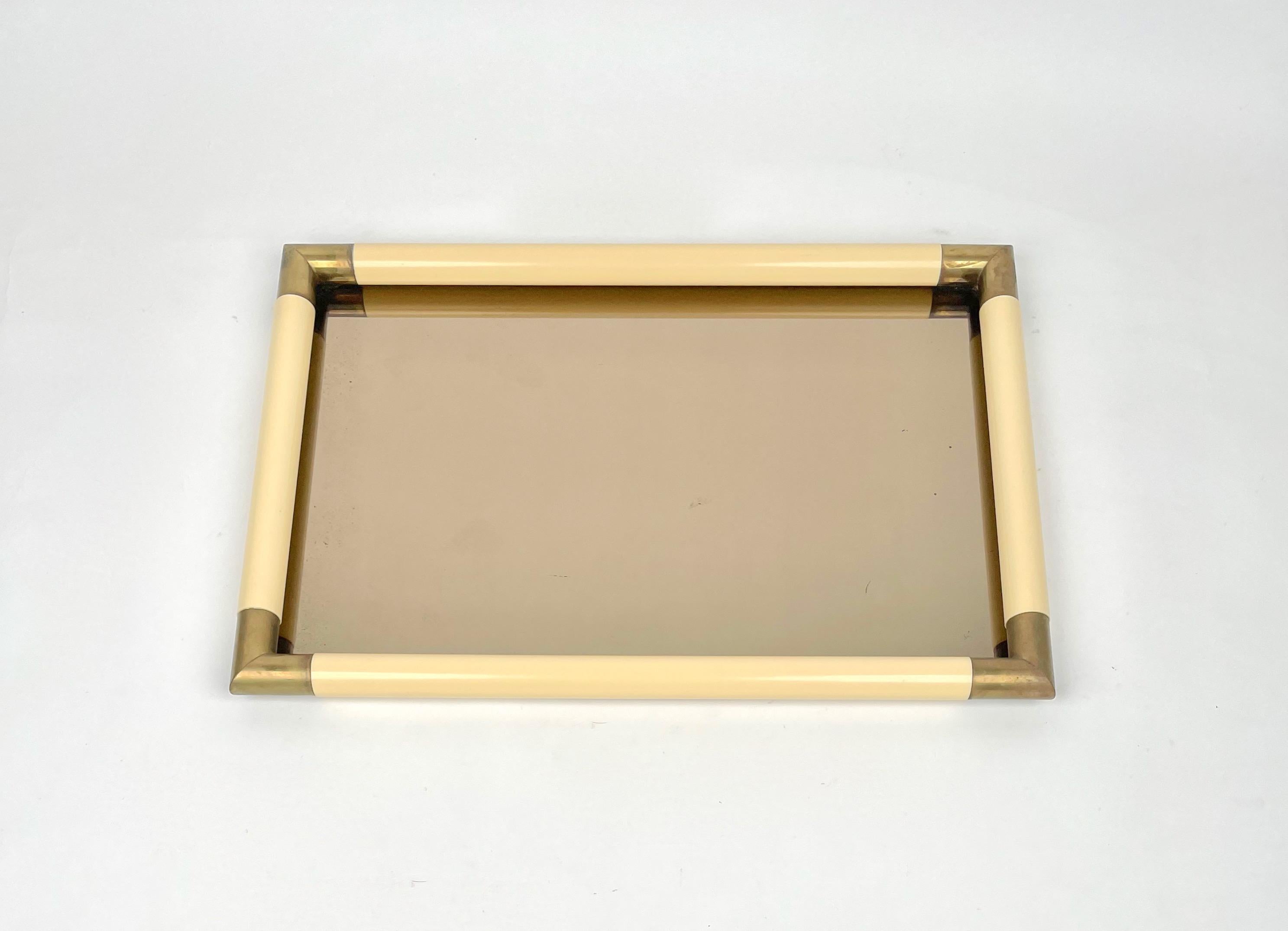 Rectangular centerpiece tray in bronzed mirror with brass corners and frame in ivory-colored plastic material by the Italian designer Tommaso Barbi. 

Made in Italy in the 1970s.