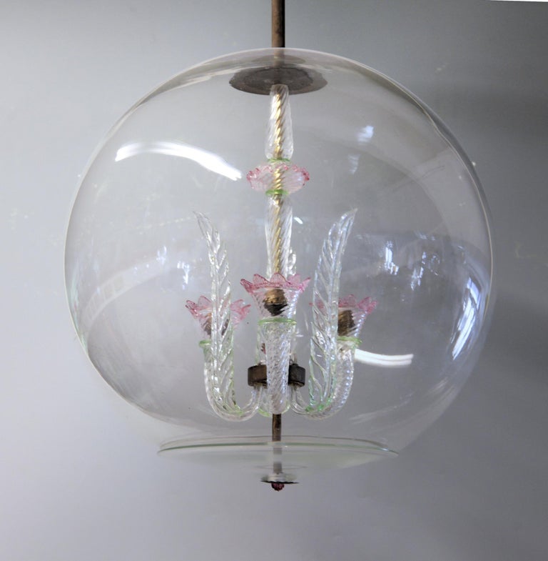 Historical Venini piece created under former director Tommaso Buzzi. 
Small glass chandelier with 3 leaves and brass hardware encased in a glass sphere with lower lid.
As far as I know, the colored version is extremely rare. There is a touch of a