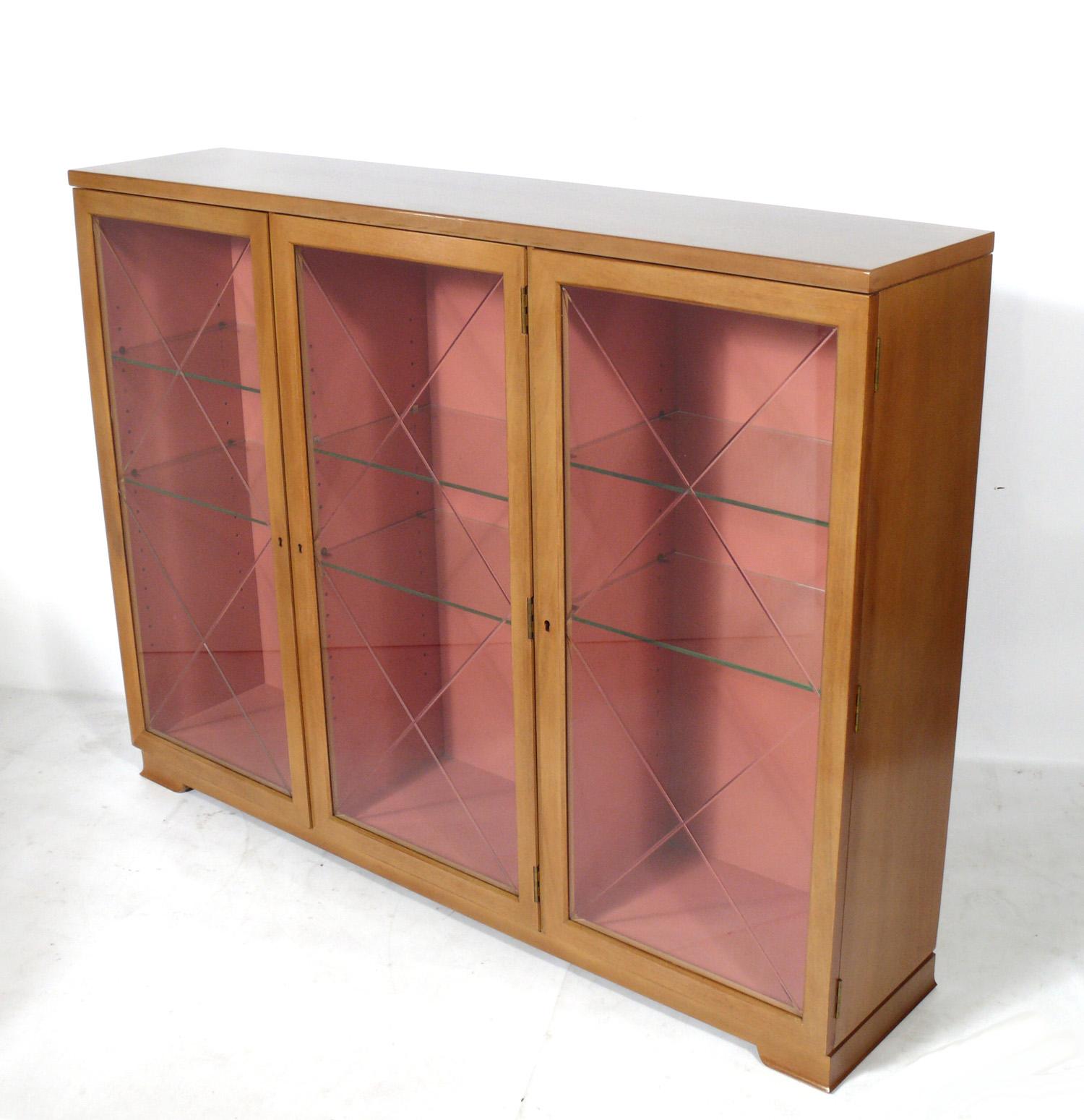 Elegant bookcase or vitrine, designed by Tommi Parzinger for Charak Modern, circa 1950s. This piece is a versatile size and can be used as a bookcase, vitrine, bar, or display case. It features three doors that open to reveal six adjustable glass