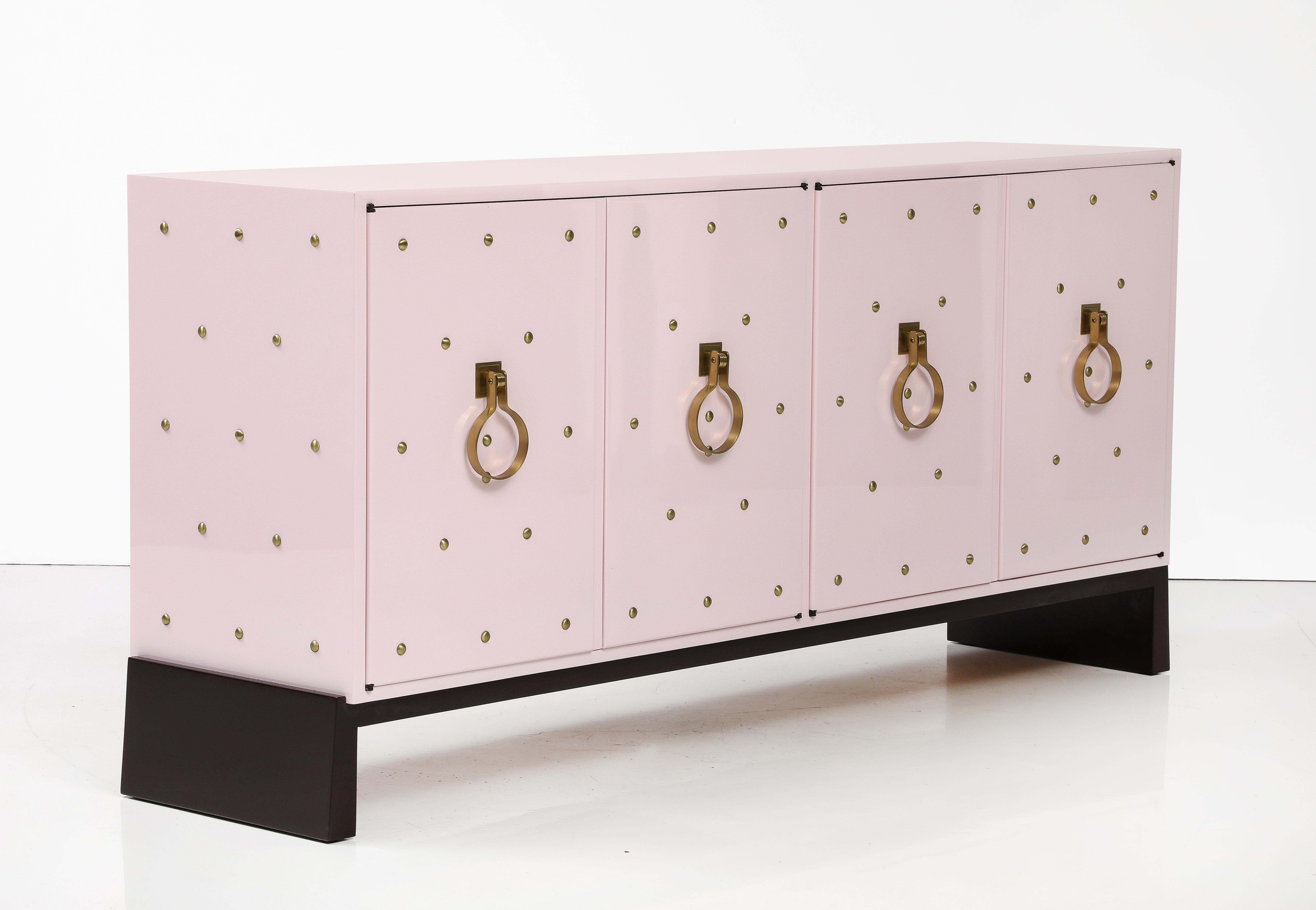 Exquisite custom Botticelli Shell Pink hand gloss lacquered credenza featuring brass studs and signature Parzinger brass door knocker pull rings. The cabinet has adjustable shelves in each compartment and a divided felt lined drawer with the