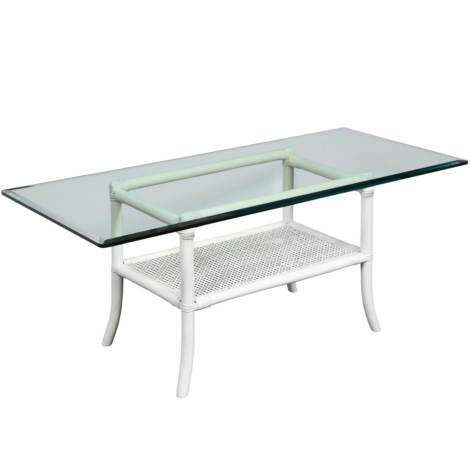Elegant white lacquered coffee table with splaying legs, beveled glass top and caned shelf by Tommi Parzinger for Willow and Reed, American 1950’s. Willow and Reed designed furniture ideal for enclosed porches or outdoor areas not exposed to the