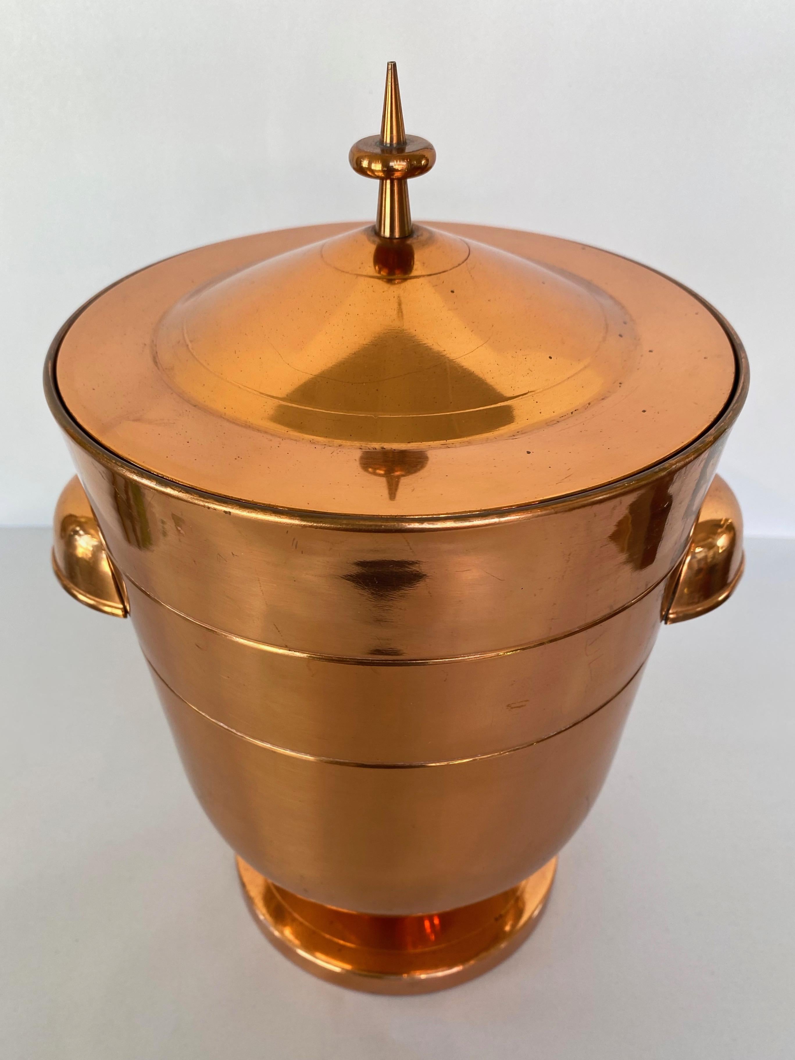 A striking 1950s rare copper ice bucket or champagne & wine cooler with lid by Tommi Parzinger.

Very seldom seen bright copper finish with protective lacquer clear coat. Lid features Parzinger’s signature spike & saucer finial detail. On a