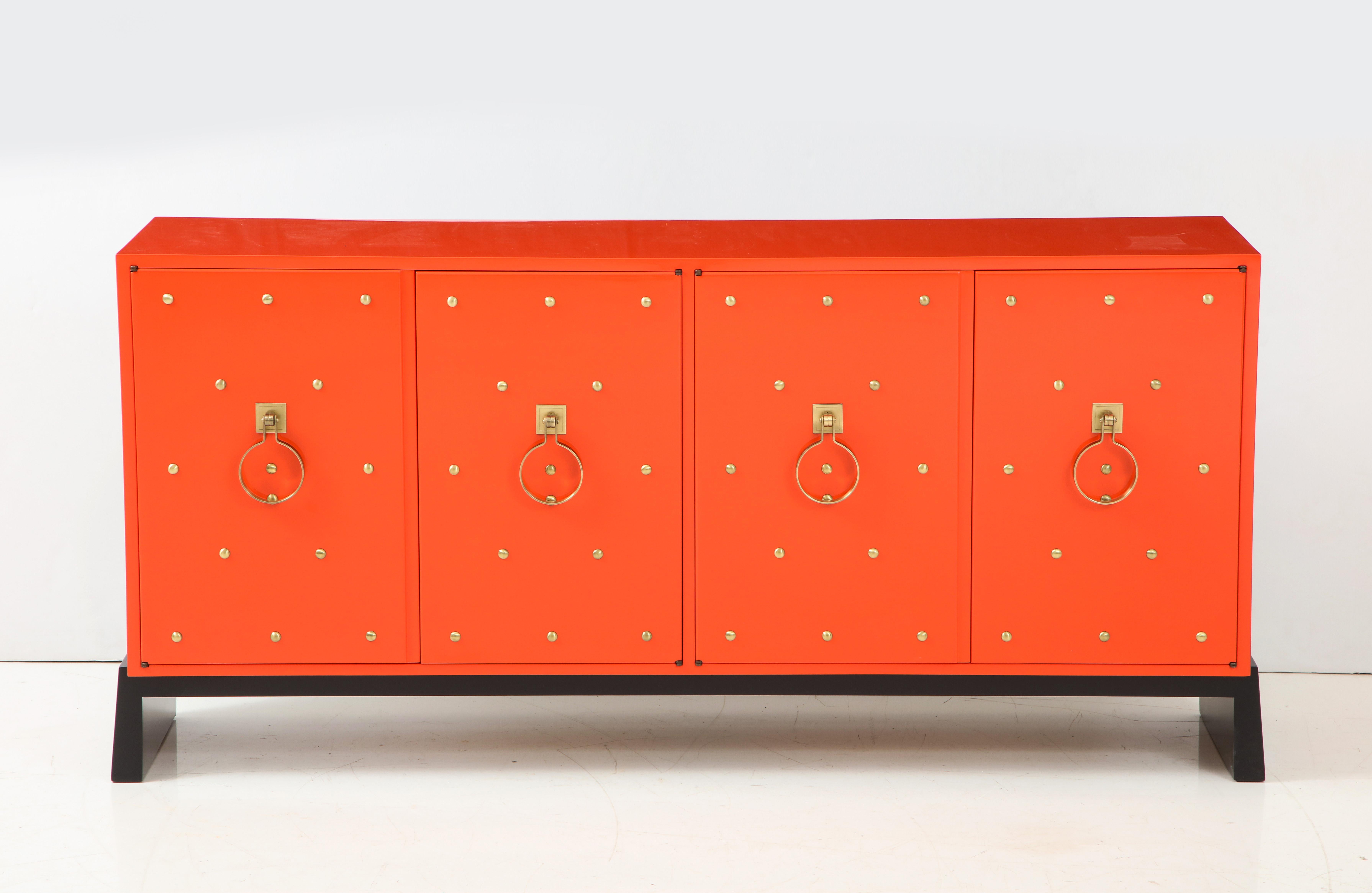 Tommi Parzinger credenza featuring 4 doors which conceal 2 storage compartments, 1 having a felt lined divided drawer, the other 2 adjustable shelves. Sideboard has been mint restored; color is based on the original coral orange color. Sides and