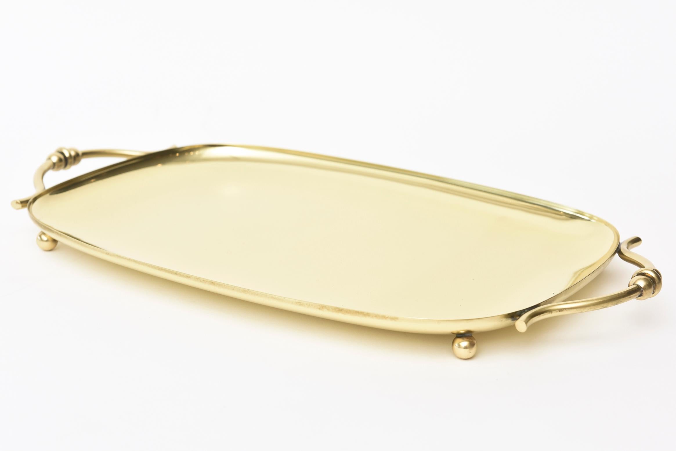 This hallmarked brass tray by Dorlyn silversmiths for Tommi Parzinger is Mid-Century Modern. The tray has 4 ball feet and curved handles at either end. It is from the 1950s and has been polished and lacquered. It is very versatile and is great
