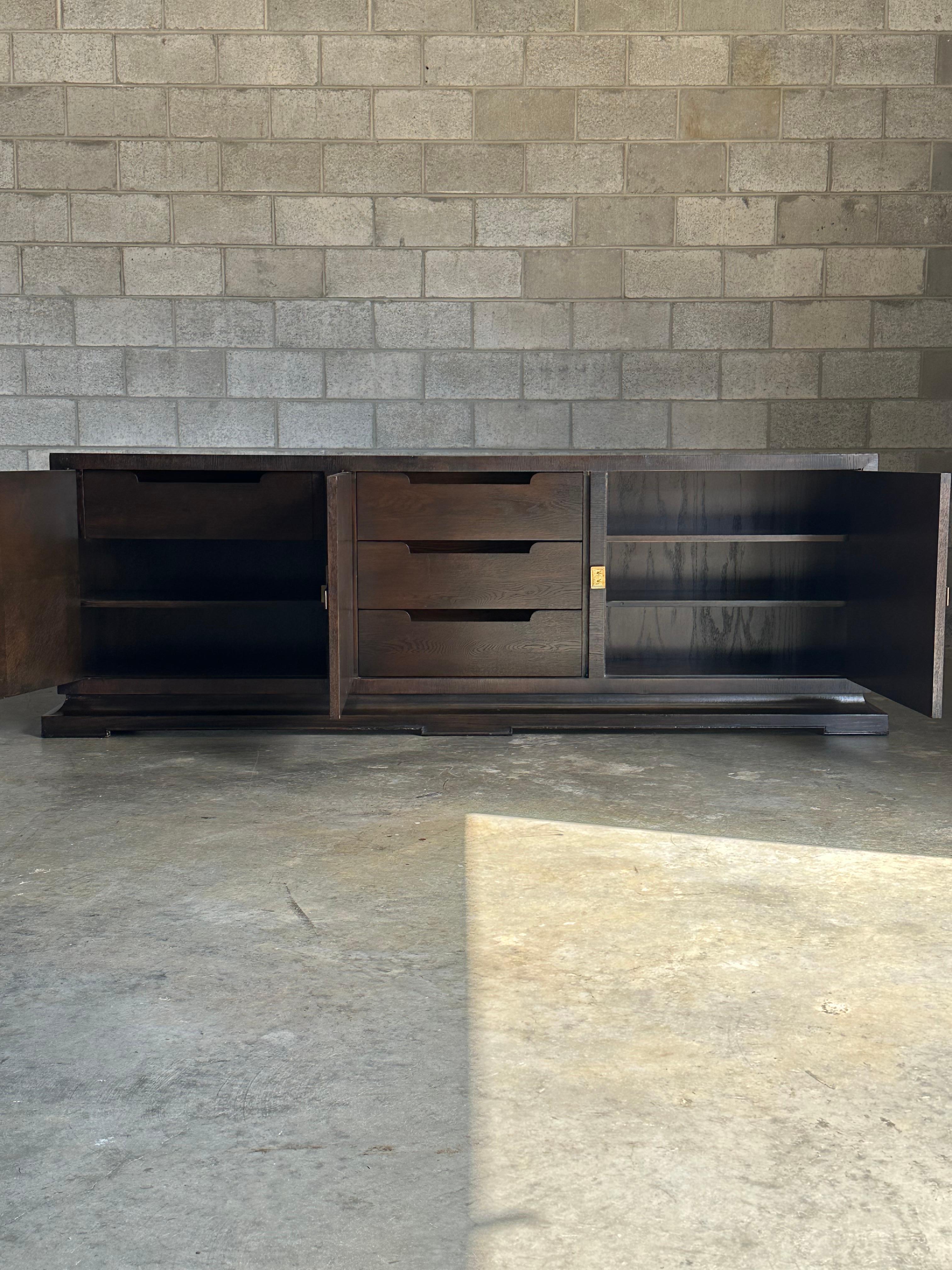 A rare long credenza designed by Tommi Parzinger for Charak Modern. Features three sections each revealed by a door. Left section containing a drawer and shelf, middle section housing three generous drawers, and right section having two shelves.