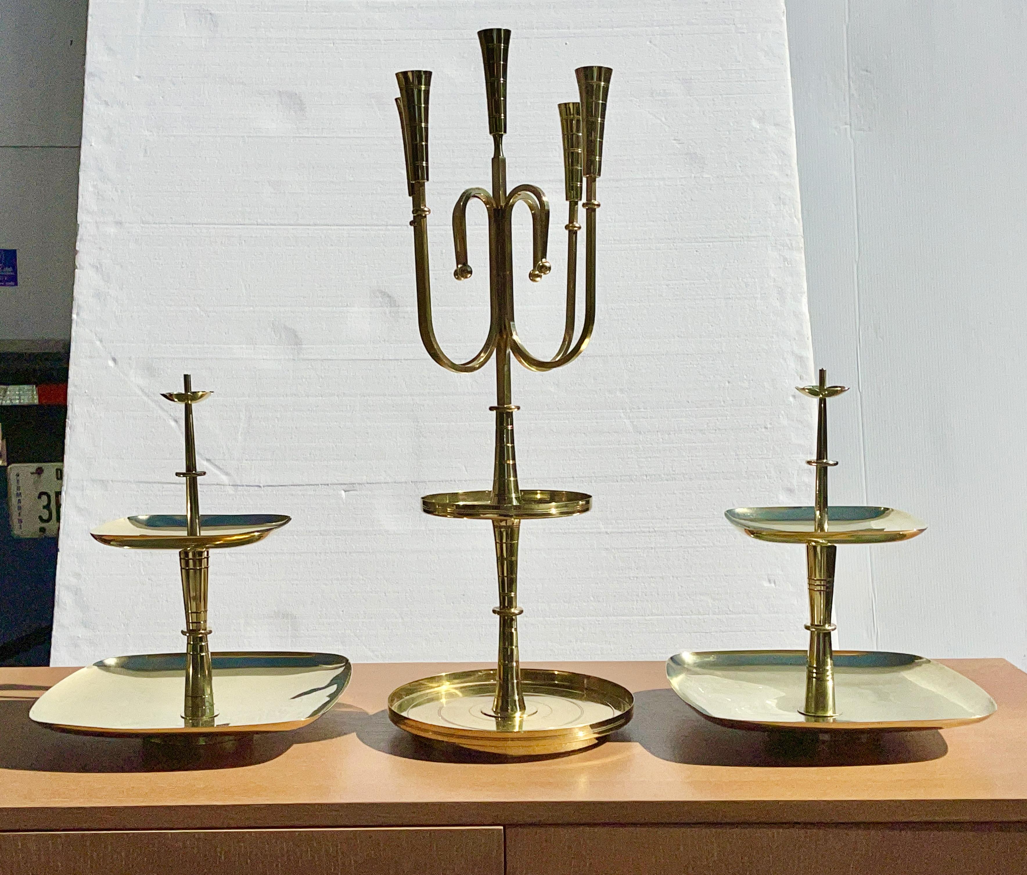 A three piece serving centerpiece grouping from among the least commonly seen items from the 1950's brass ware collection designed by Tommi Parzinger for Dorlyn Silversmiths, consisting of an exceptionally large candelabrum for five tapers with two