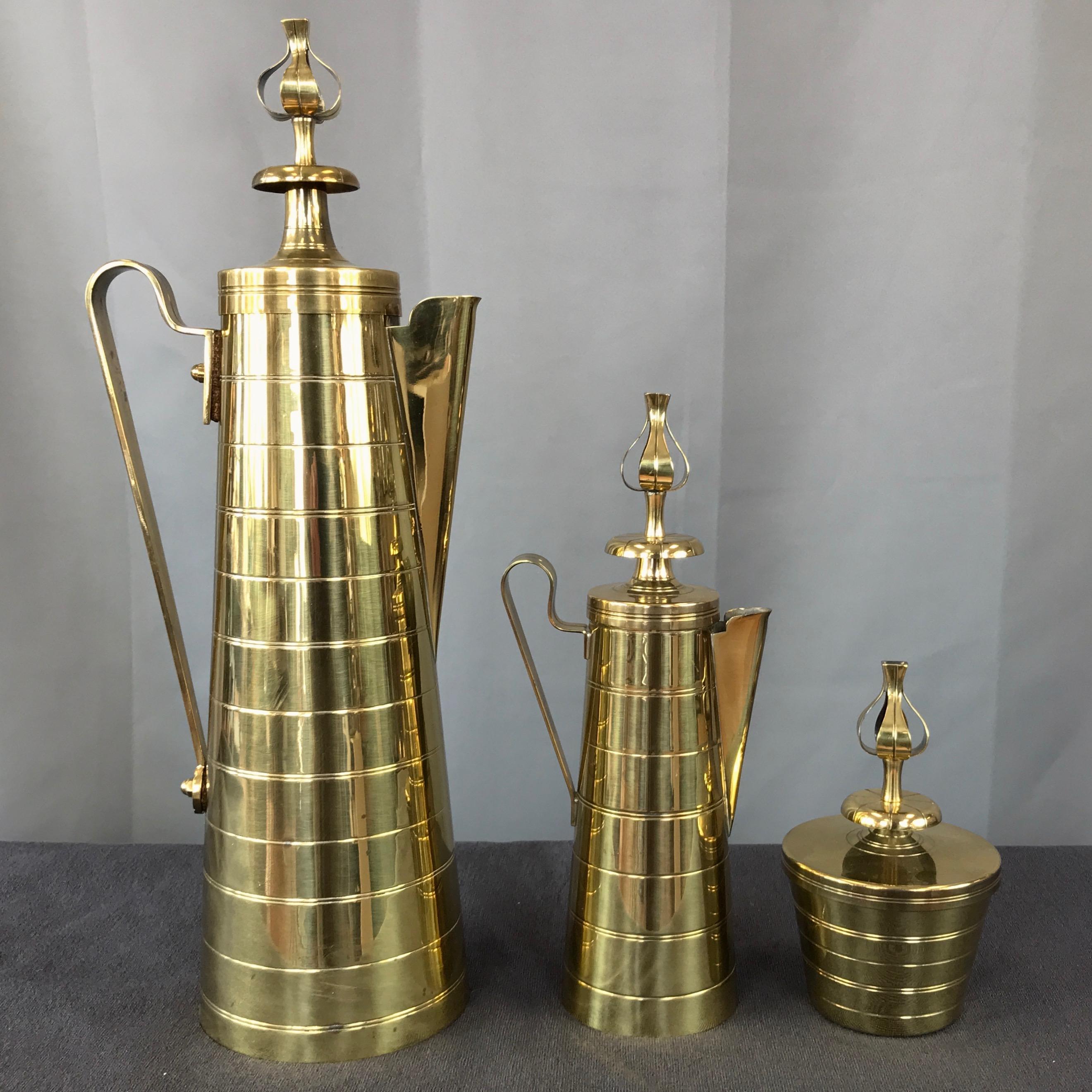 A stunning Hollywood Regency three-piece brass coffee service by Tommi Parzinger for Dorlyn Silversmiths.

Polished solid brass set comprised of a statuesque carafe, matching creamer, and generous sugar bowl, all with regal multi-tiered lids. Each