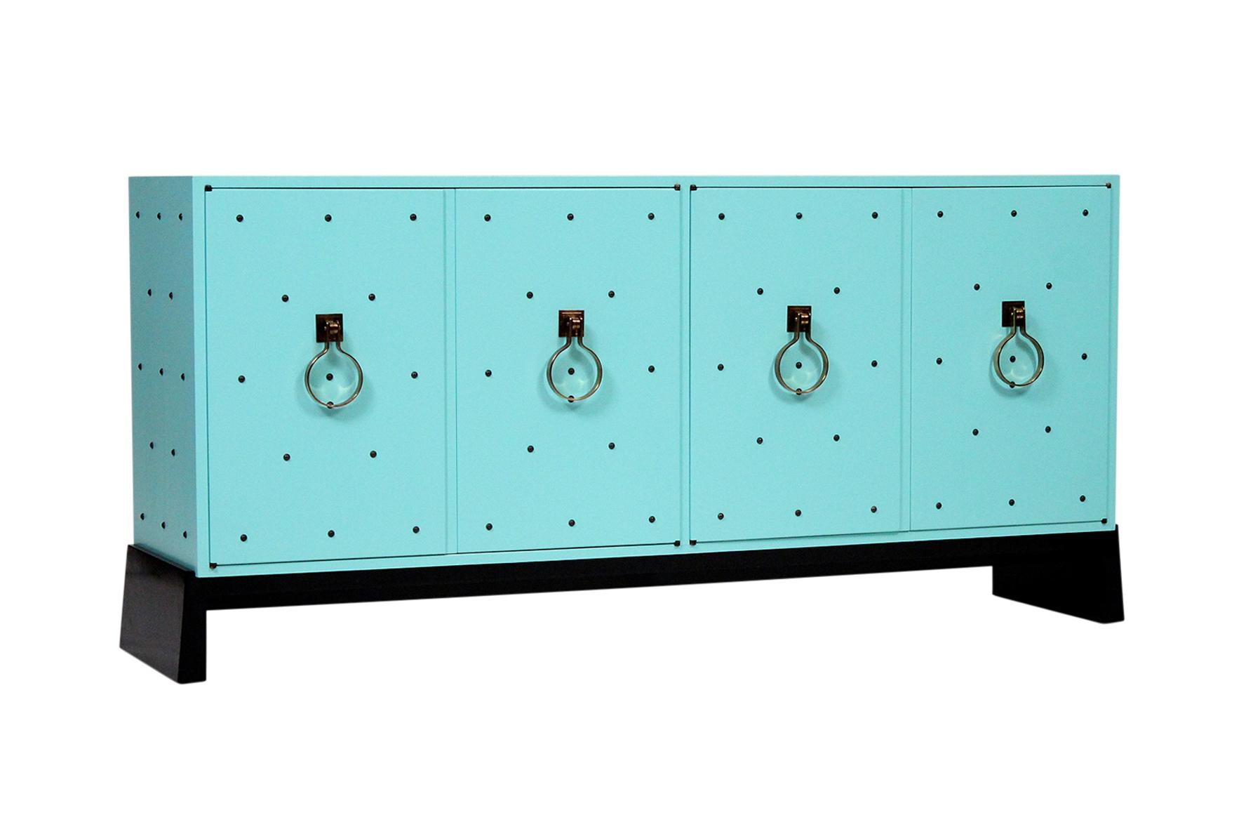 Tommi Parzinger for Parzinger Originals lacquered in Robins Egg blue exterior and a white interior. Cabinet on a lacquered black base. Four doors with brass studs and pulls. Open storage on left and drawer and shelving on right.
 Signed.