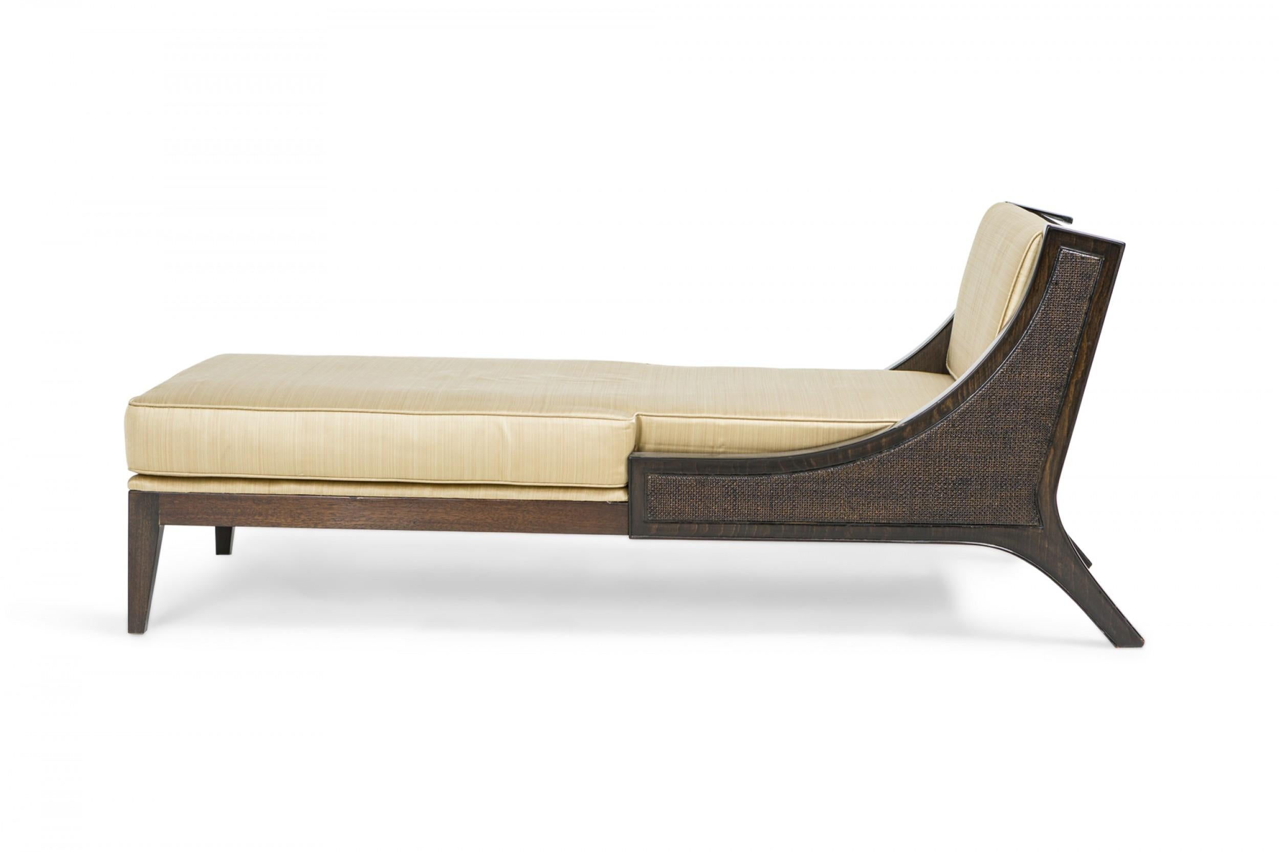 German mid-century chaise lounge with an ebonized wooden frame with caned sides and back, and back and seat cushions upholstered in gold satin fabric. (Tommi Parzinger).