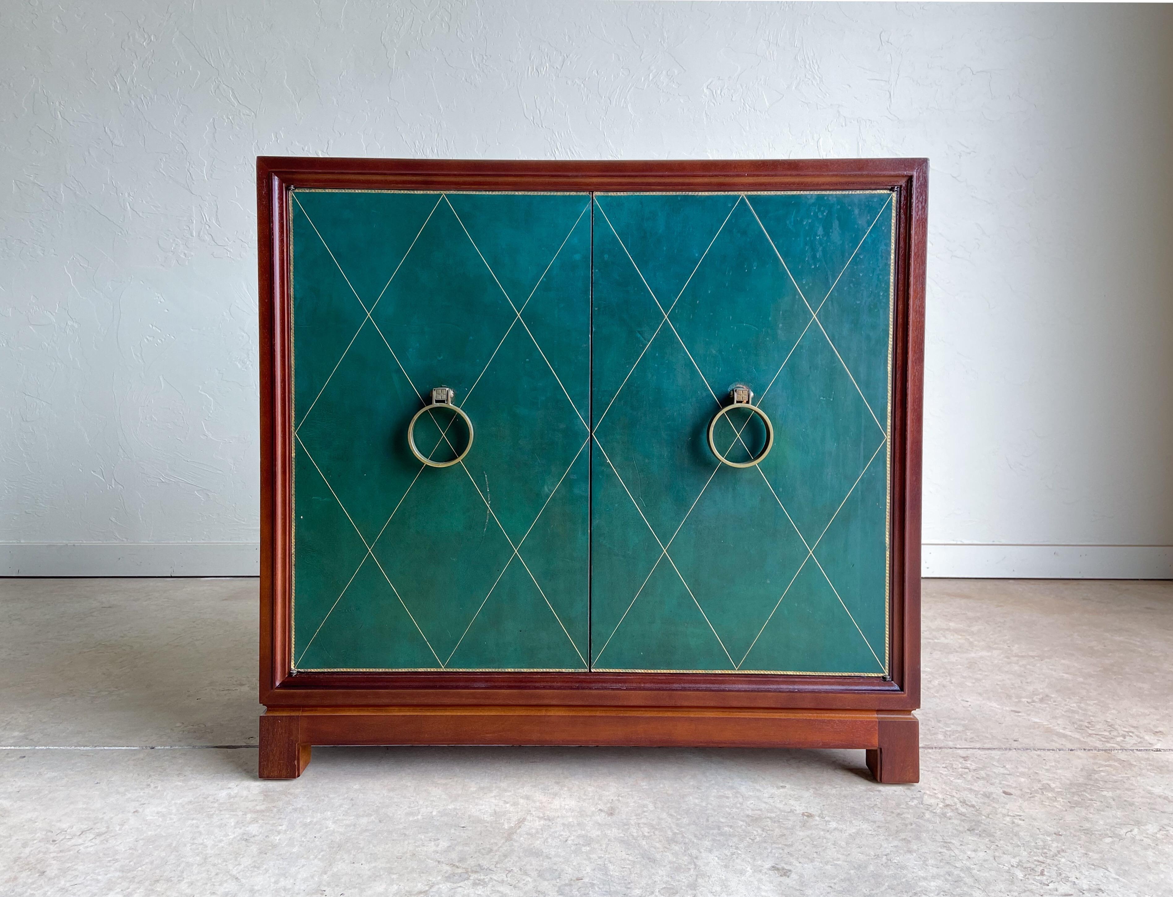 Offered is a somewhat uncommon cabinet designed by Tommi Parzinger and produced by Charak Modern. 

Featuring mahogany wood construction in a lovely dark brown finish. The dark green leather doors are accented with a beautiful geometric gold inlay
