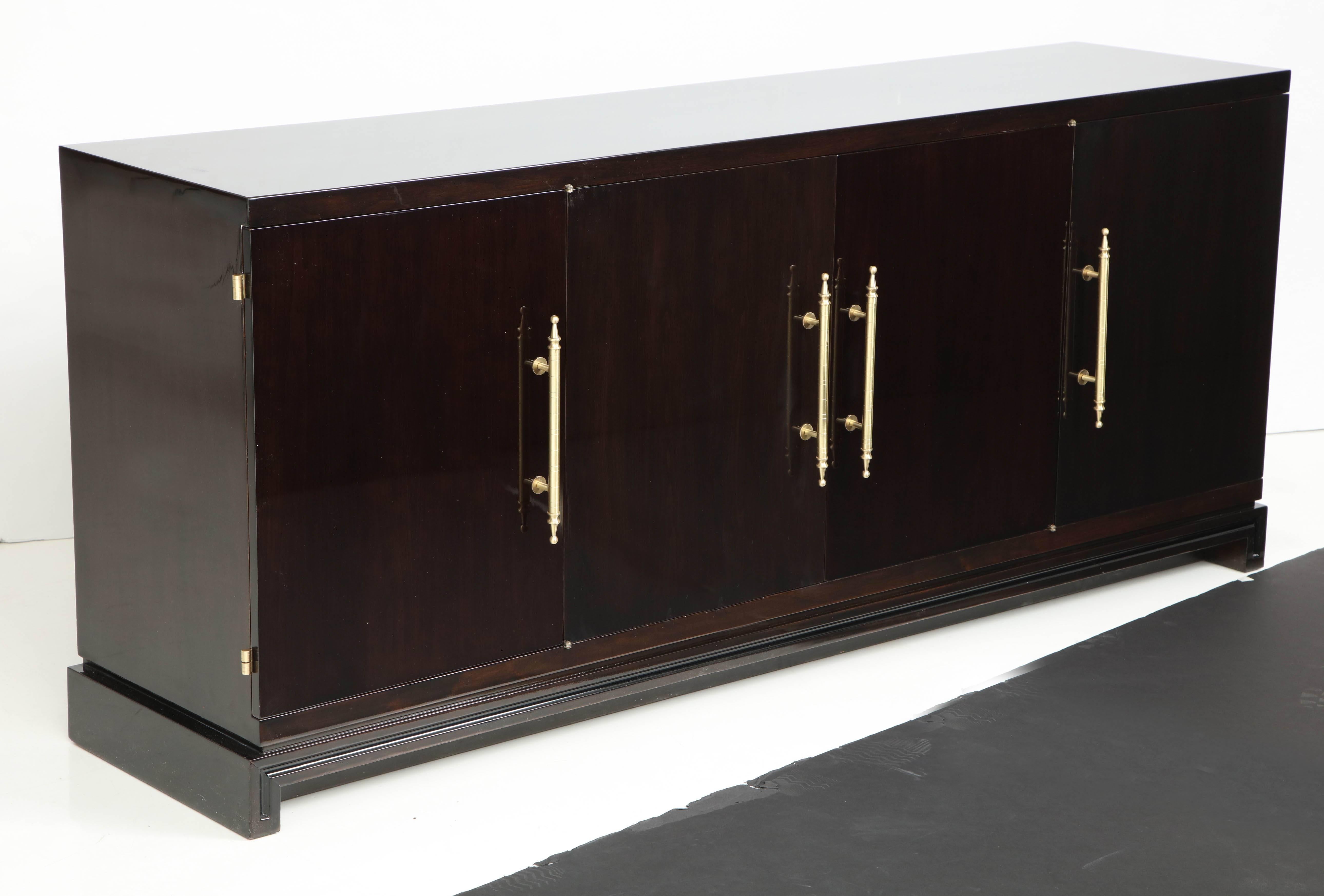 Refined and tailored midcentury Classic ebonized mahogany credenza with a three storage compartments, the center compartment housing two drawers and a shelf, the outer compartments having adjustable shelves. The case is a rich dark brown with a