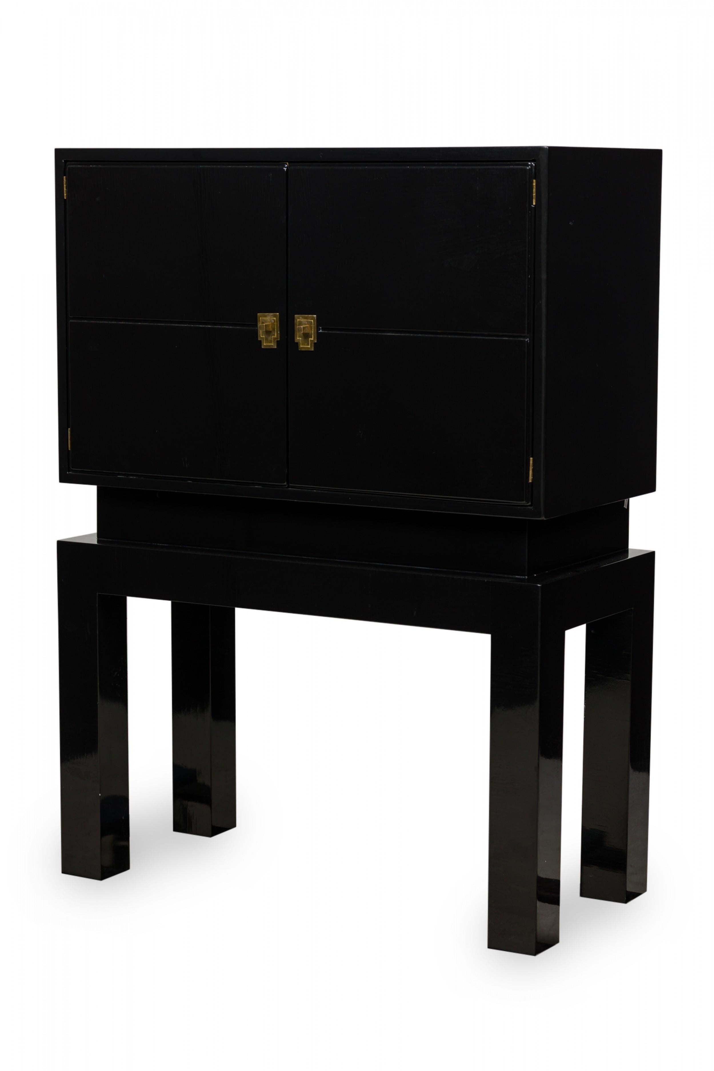 Tommi Parzinger midcentury (1970s) American Modern black lacquered rectangular bar cabinet in a Brutalist form features 2 hinged doors (with stylized bronze pulls) opening to reveal a 2-shelved storage compartment, standing on 4-legged block frame.
