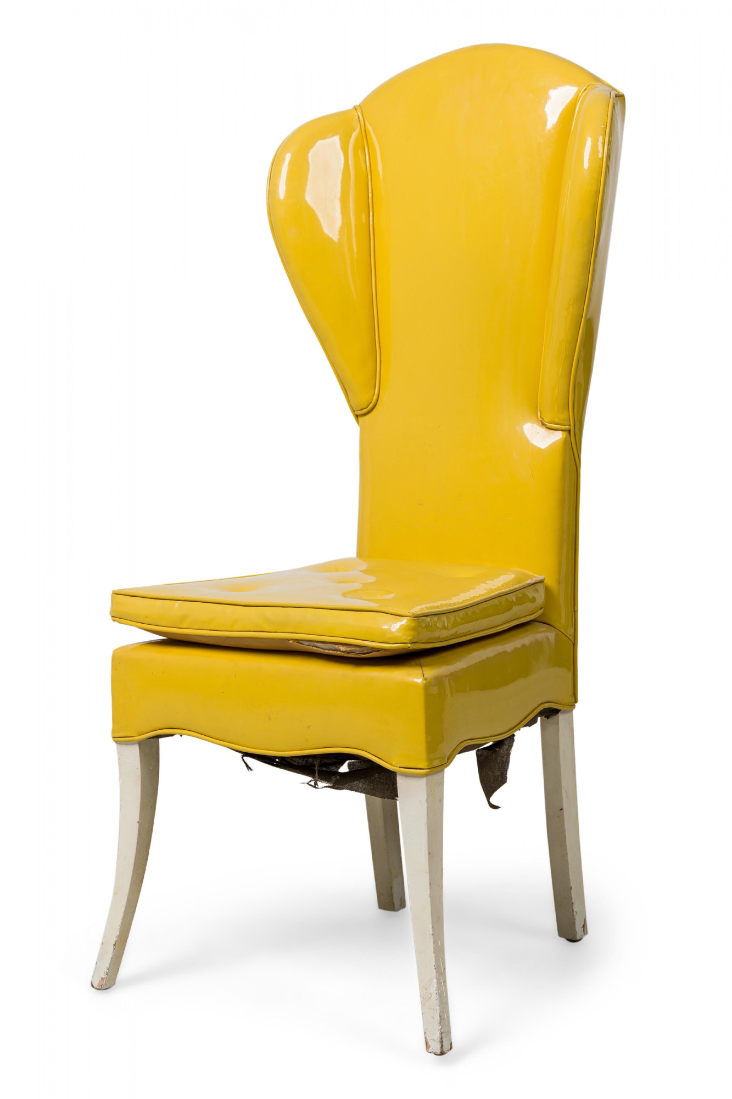 Midcentury American wing chair, padded and upholstered in glossy yellow vinyl with a square seat cushion, shaped apron and white painted splayed legs. (Attibuted to Tommi Parzinger).
