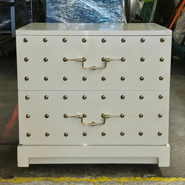 Tommy Parzinger for Parzinger Originals white lacquered two drawer cabinet. 
Some call this a dresser but scale suggests nightstand or bedside chest.
Solid brass round domed studs evocative of hobnail and quintessentially Parzinger refined drawer