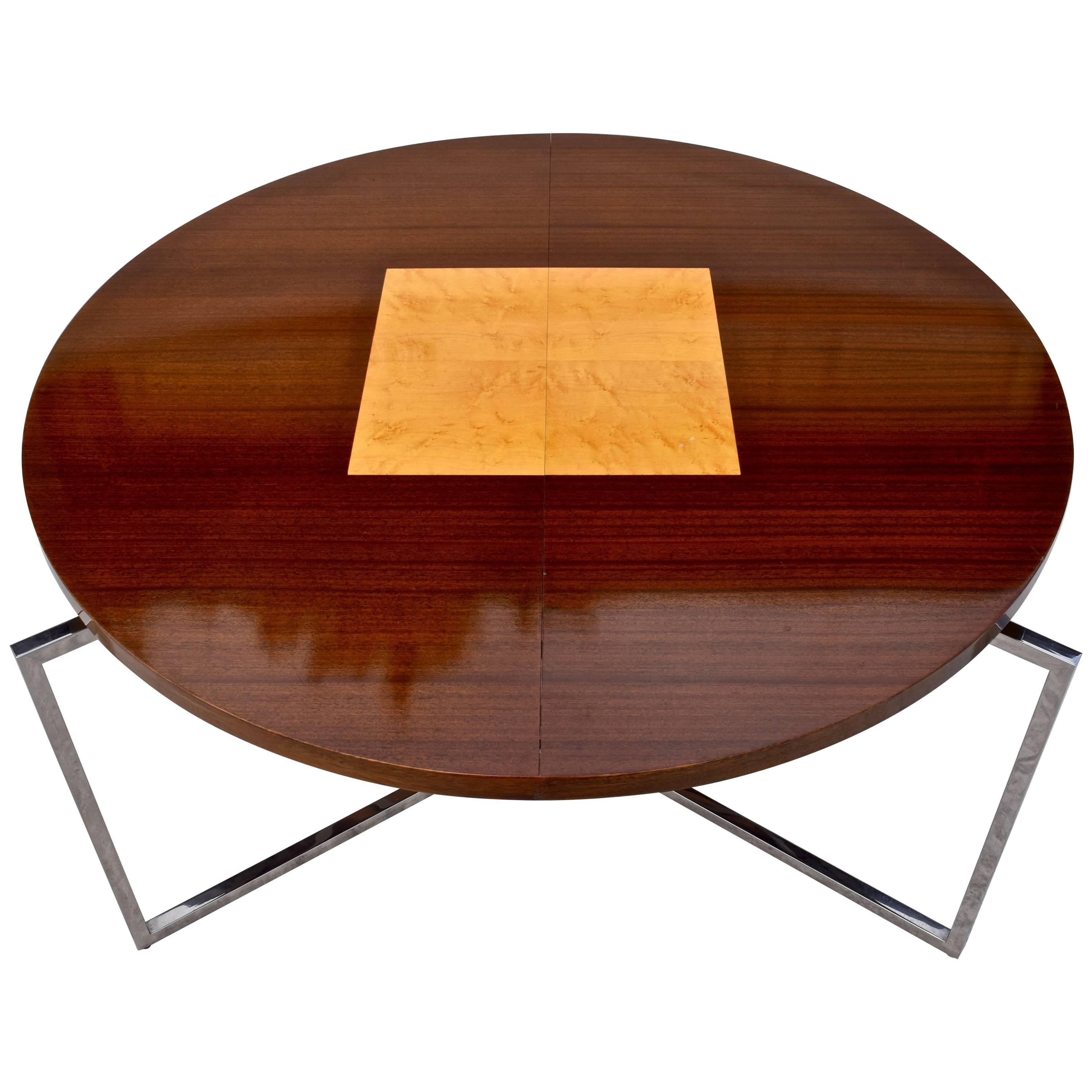 Tommi Parzinger originals dining table model number 701 supported by a chrome frame which extends beyond the round top. When the two leaves are inserted the legs are under the table. The mahogany top has a bird's-eye maple square insert in the