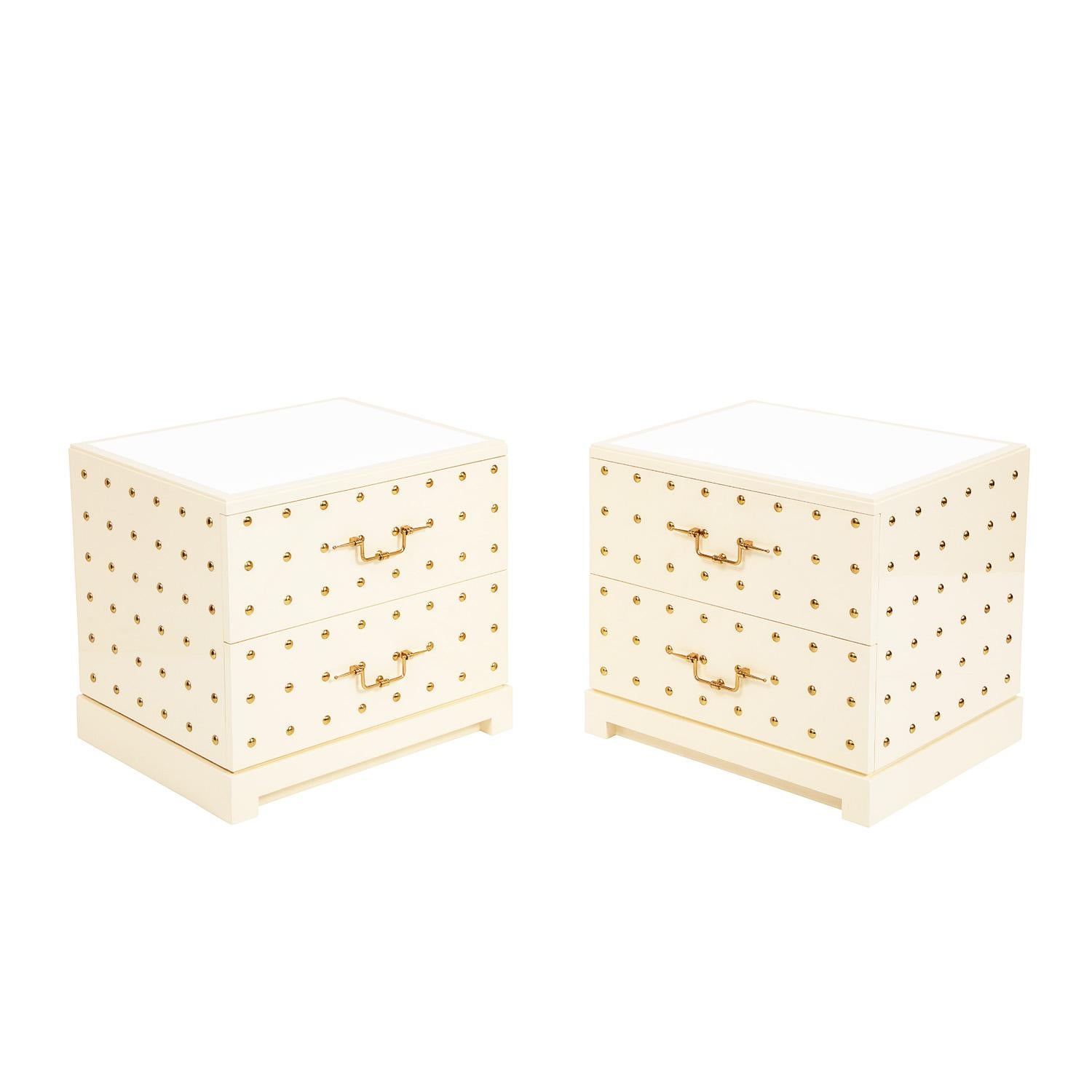 Pair of bedside tables model 223S, each with 2 drawers, in bone lacquer with original white glass tops and brass studs by Tommi Parzinger for Parzinger Originals, American 1950's. These bedside tables are rare and exude the glamor and elegance that