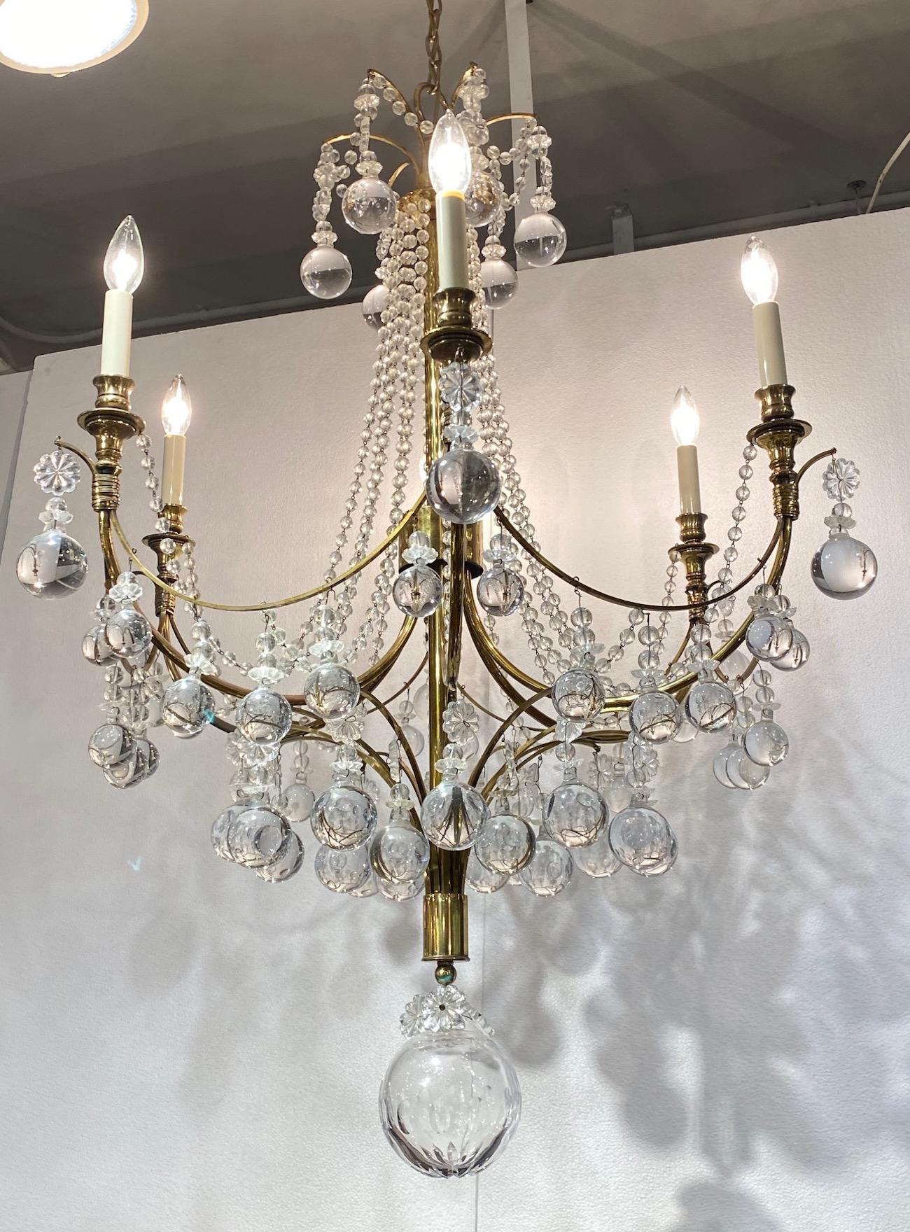 An elegant and large 1950s Hollywood Regency six light chandelier in the style of American designer Tommi Parzinger. Brass with cut crystal bead swags, glass ball drops and rosettes. Lovely attention to detail with wrapped brass band ornament below
