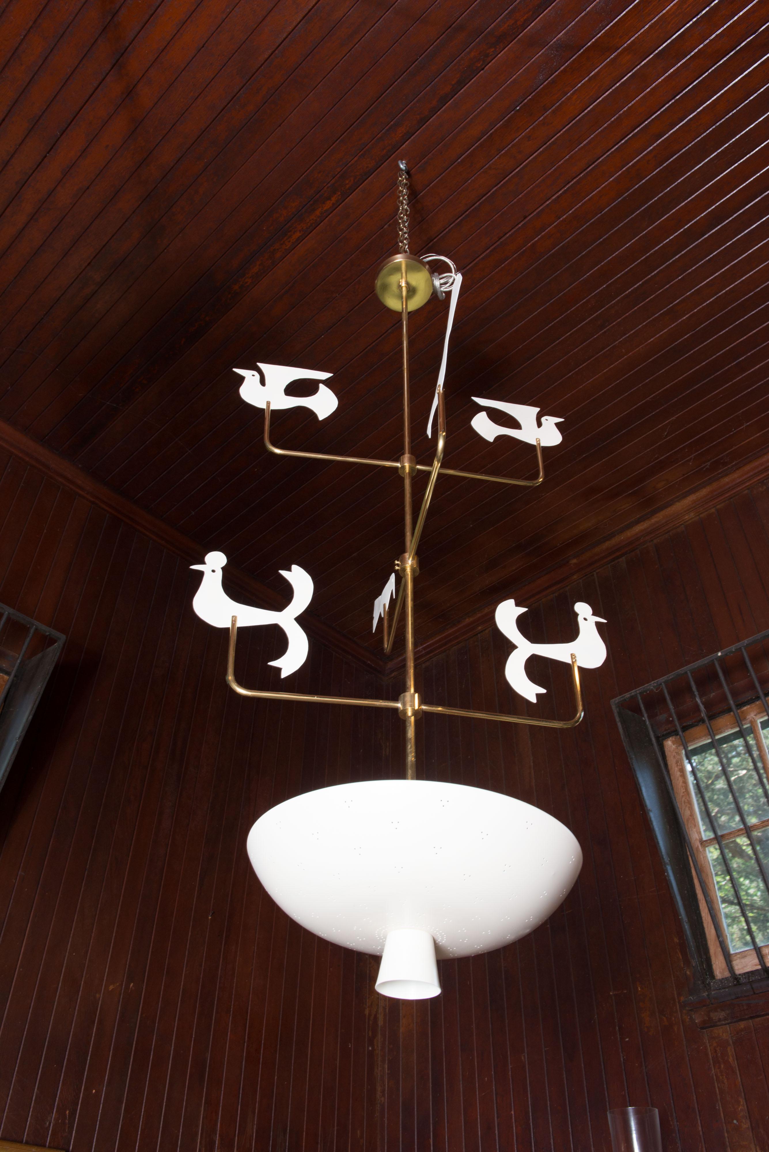 This is a spectacular custom handcrafted Tommi Parzinger inspired whimsical bird chandelier. The sleek white enameled aluminum pierced shallow bowl shaped light fixture contains three standard light bulb sockets. Above the lighted bowl is a long