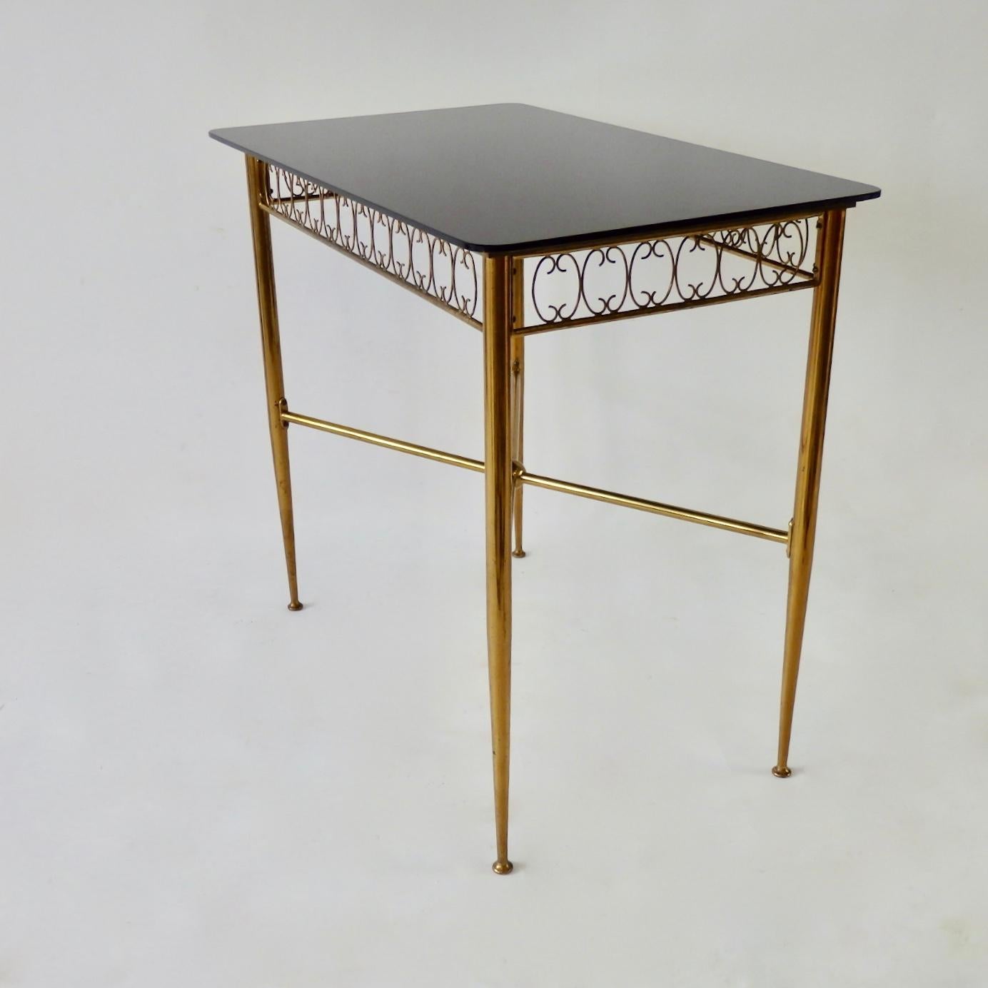 Elegant console or entry way table in the manner of Tommy Parzinger . Very possibly Italian made brass base table. Black Vitrolite glass top. Shown in natural Patina . 