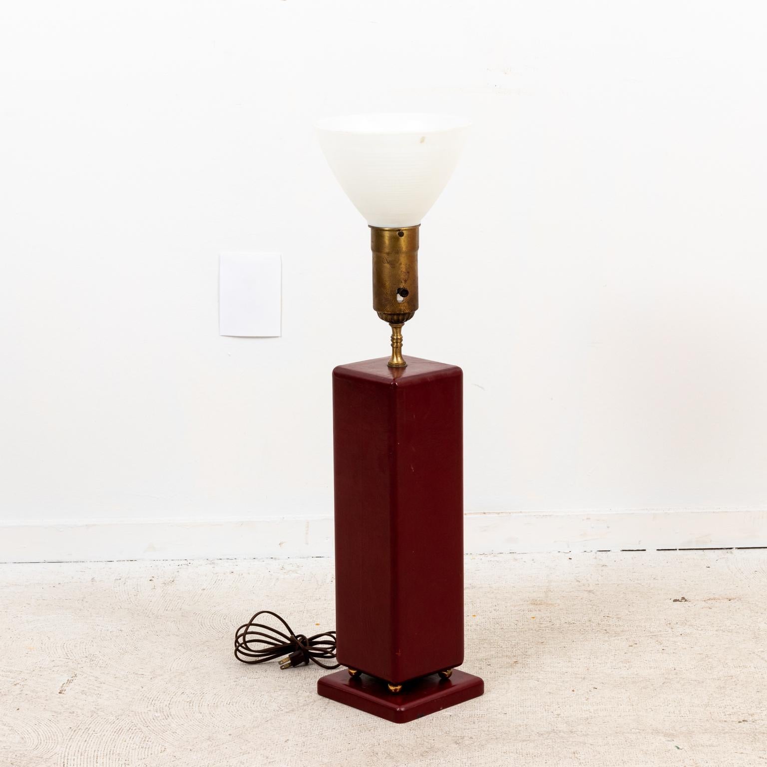Circa 1950s Tommi Parzinger style red leather table lamps. The square body is supported by four brass balls on a larger square base. Electrified. Please note of wear consistent with age including very small wear to one side of the lamp. Needs to be