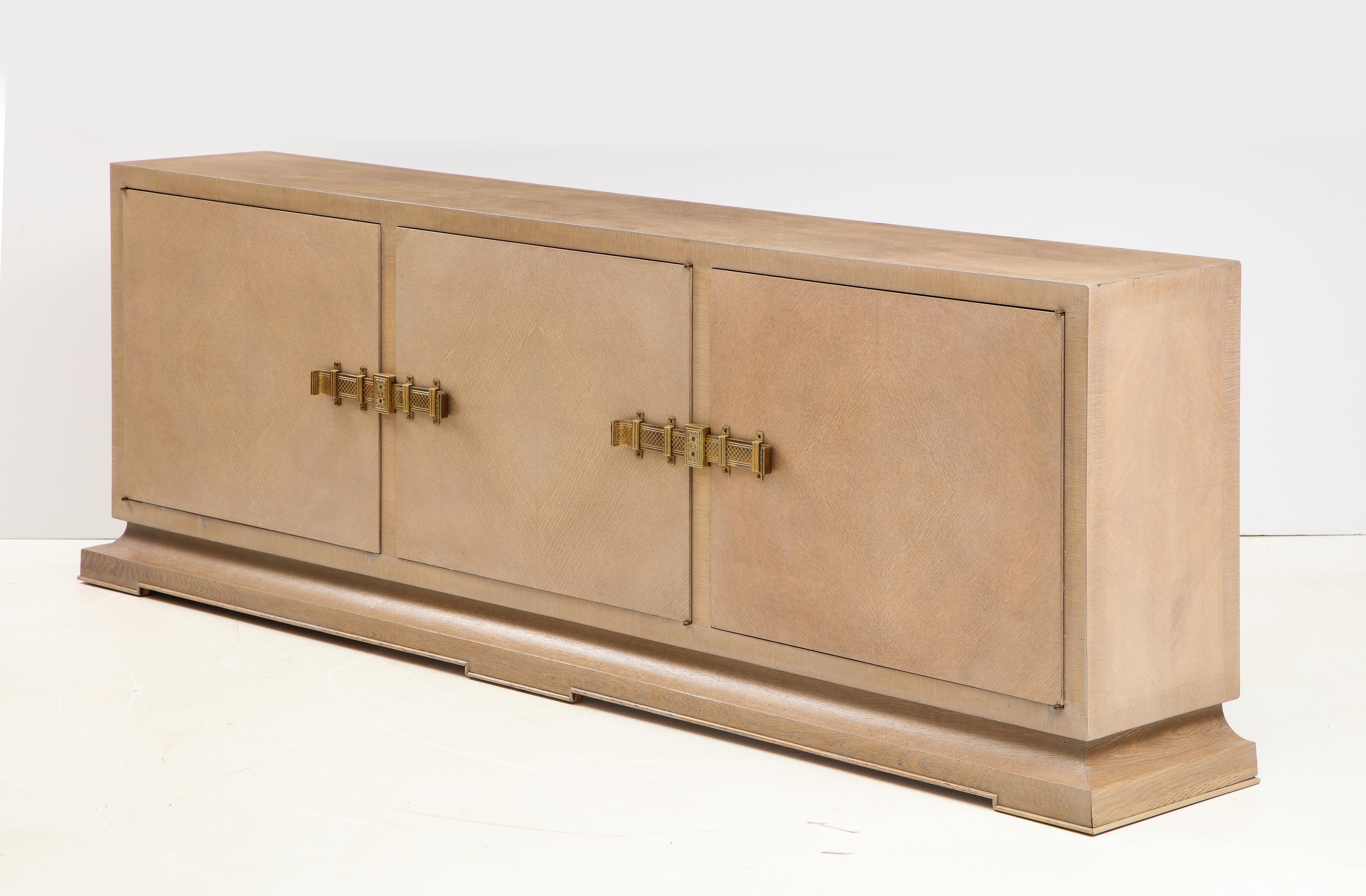 Mid-Century Modern classically styled credenza, buffet featuring a custom weathered oak/driftwood finish with aged bronzed brass hardware. Credenza has 3 sections with adjustable shelves and a center drawer. 
Refinished Condition. Tommi Parzinger