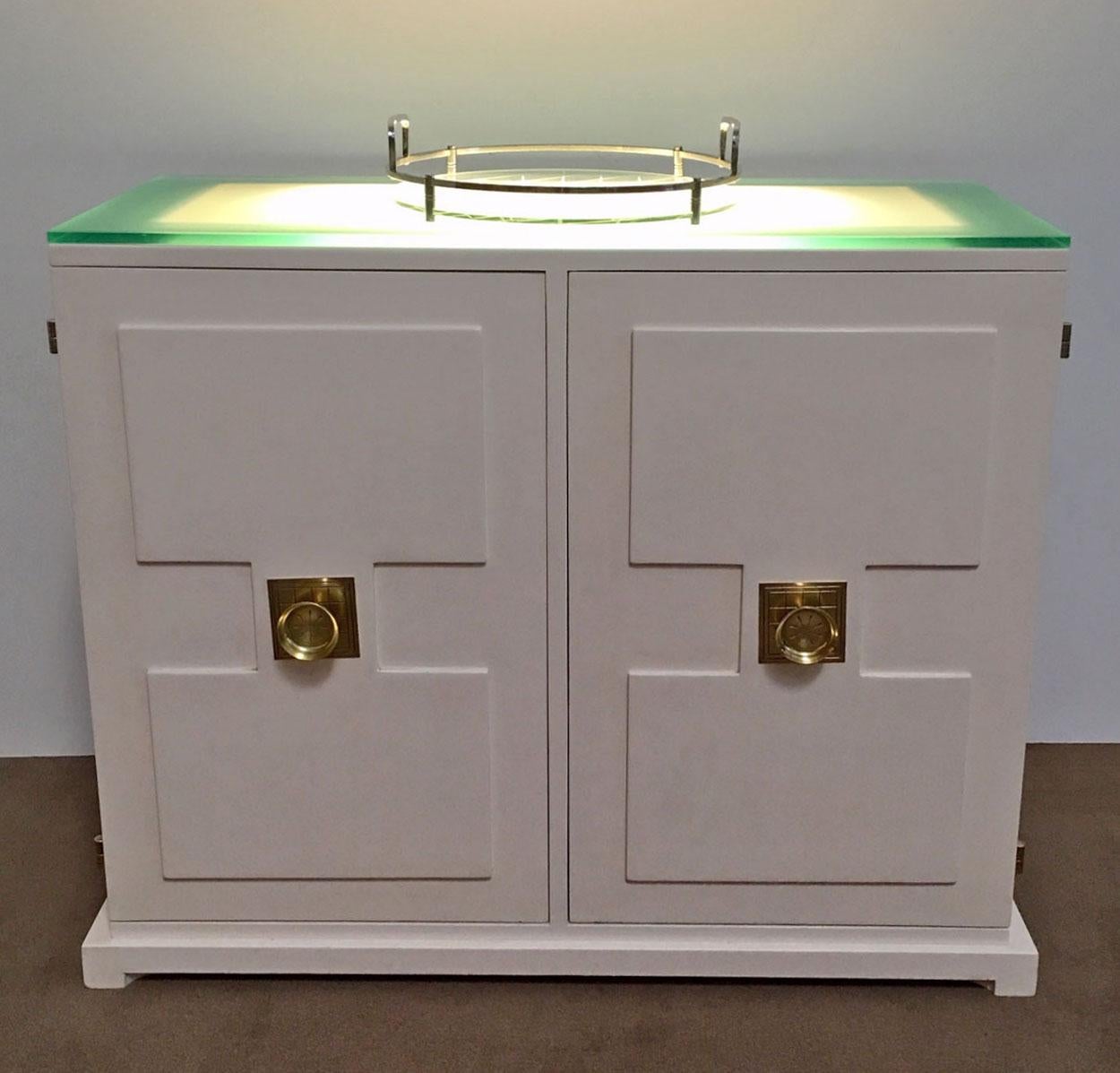 Illuminated two-door bar cabinet designed by Tommi Parzinger. Features a frosted glass top that lights from underneath, two drawers, and adjustable shelves for storage. Handles and hinges are brass. This is a beautiful example of Parzinger's design.