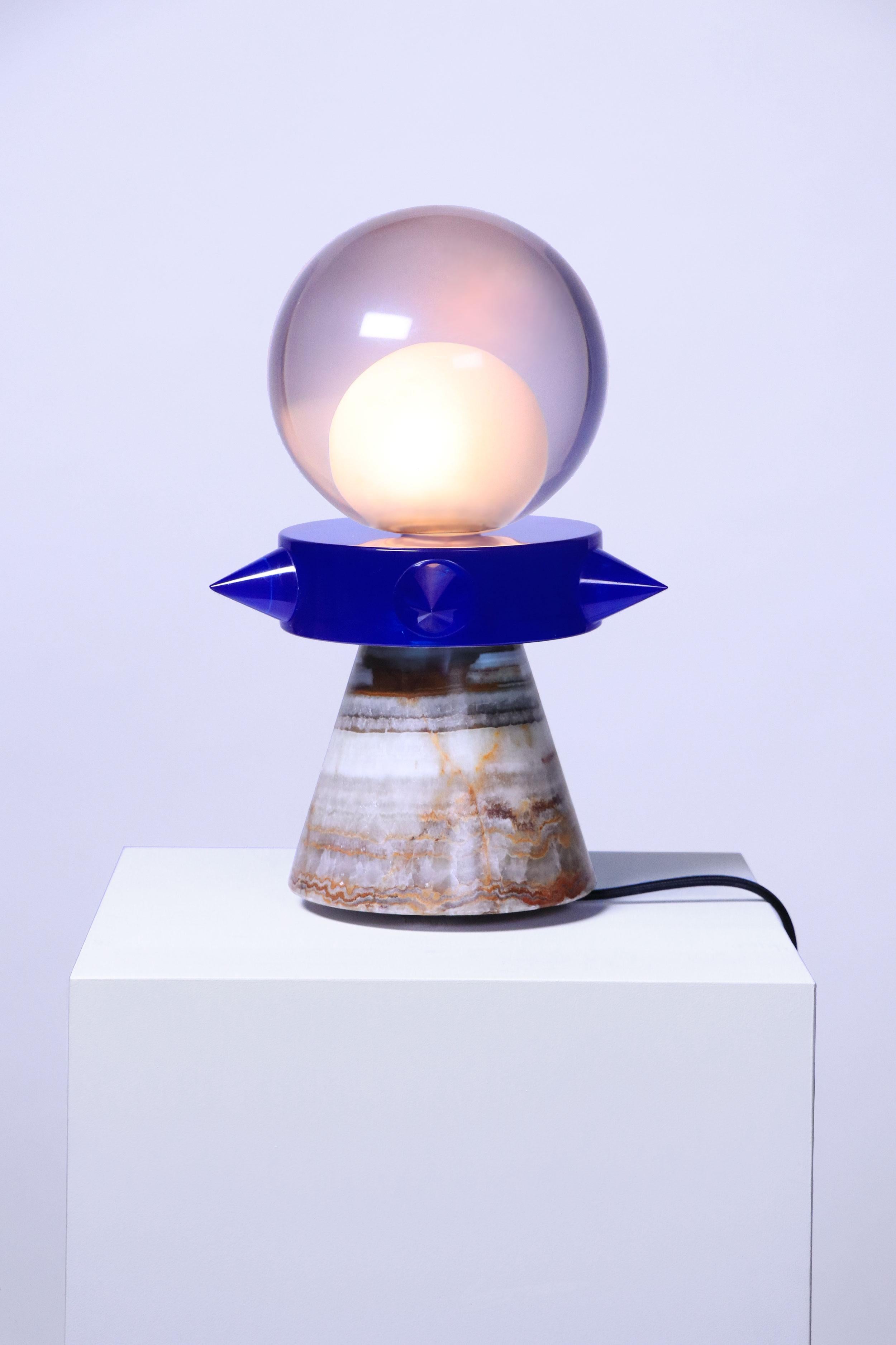 An architectural representation of the female's body. Composed of a studded collar and a light bulb. The pedestal is sculpted in Mexican onyx. Due to craftsmanship of the resin and the infinite colored veins of the onyx, each piece is