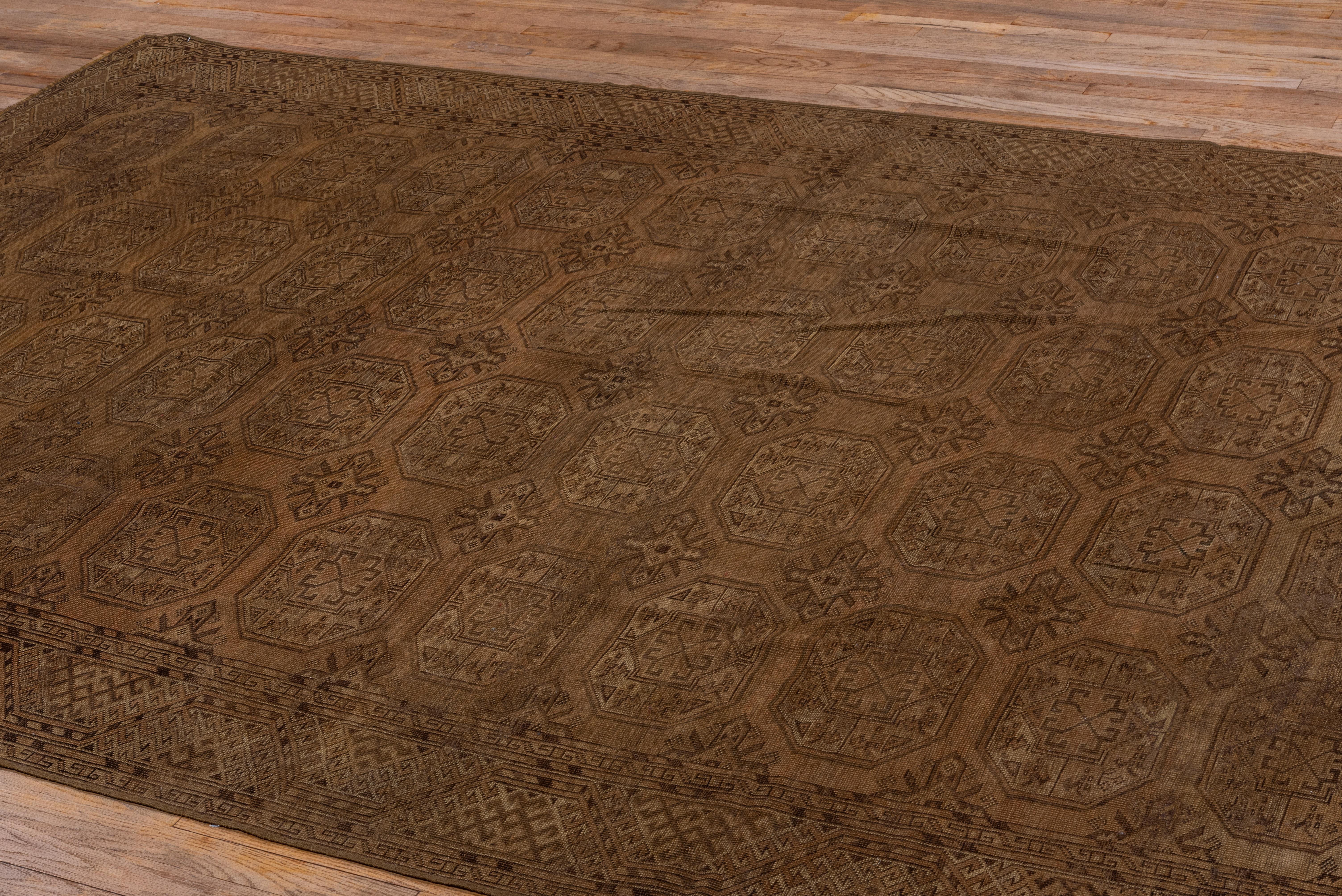 This moderate/coarsely woven all wool nomadic carpet from Central Asia show four columns of twelve octagonal Turkmen guls with chemche minor guls, on the brownfield. Faceted 