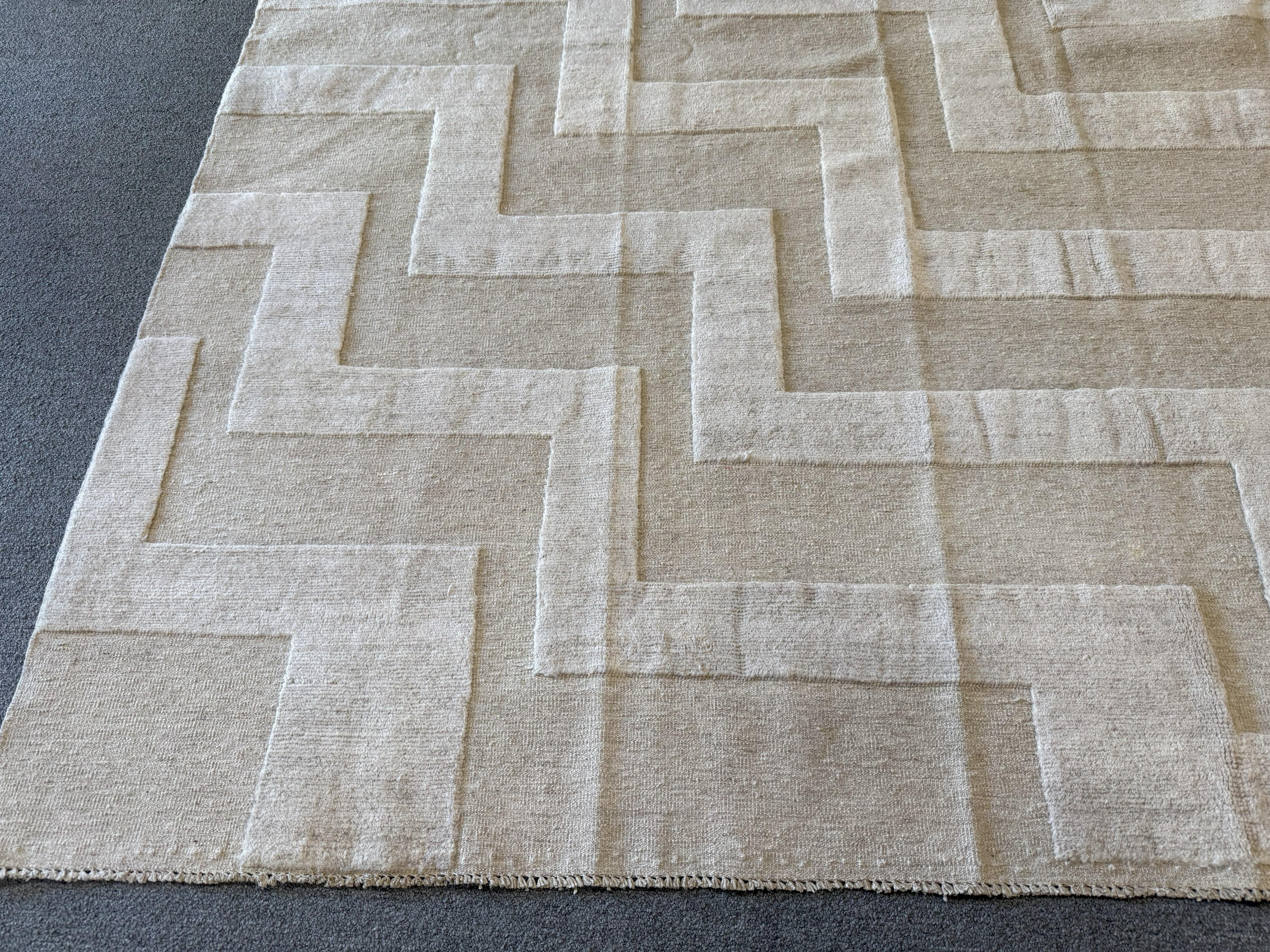 This 8'x10' tone on tone beige Pakistani rug is an elegant and graceful example of a contemporary style rug featuring intricately woven lines to form a modern design. Durable all wool construction. Hand knotted in Pakistan.