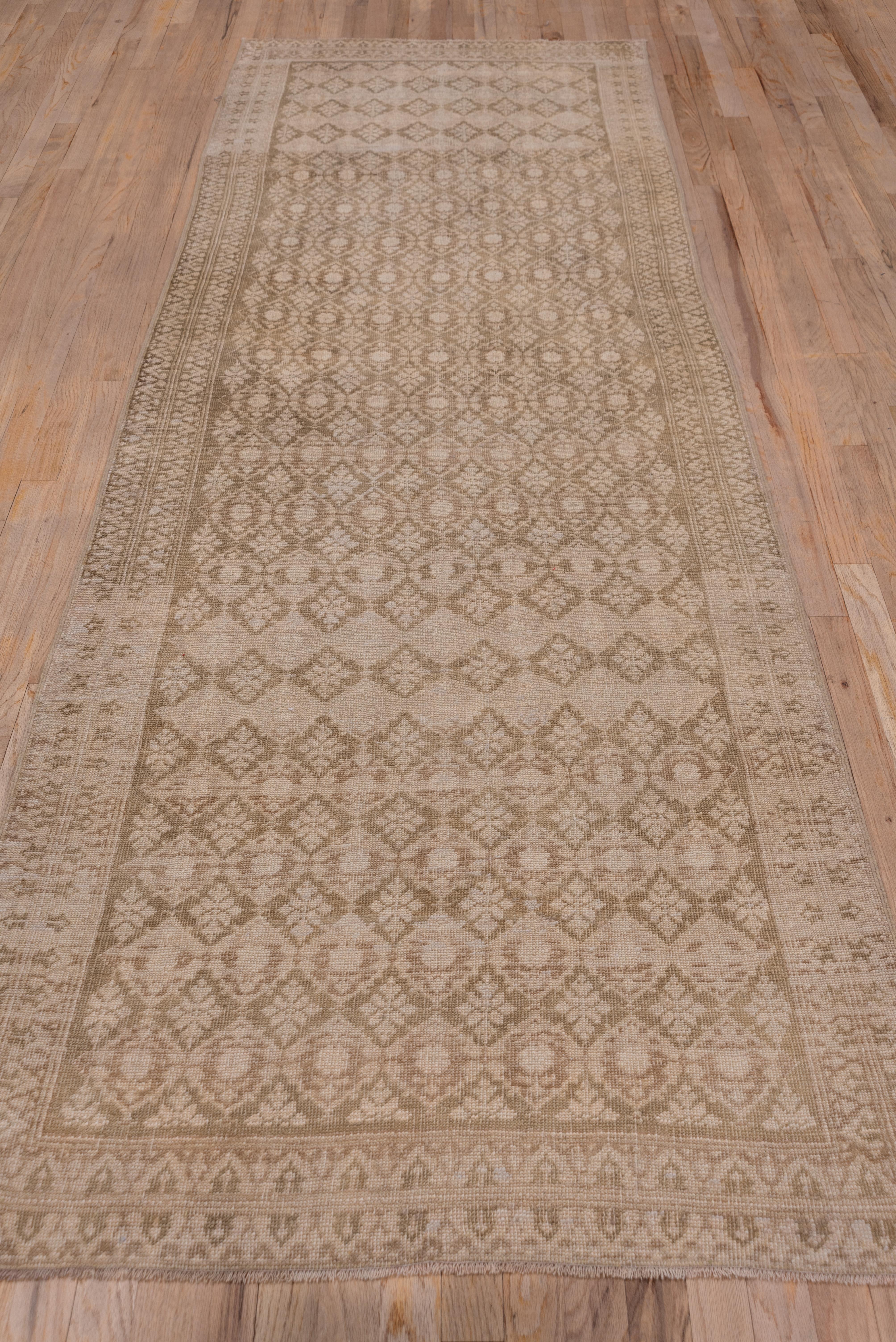 This Anatolian village runner presents a bi tonal pattern in beige and light brown of a rough lozenge lattice enclosing small leafy elements, within a double heart border. This runner has a very distinct abrash.
