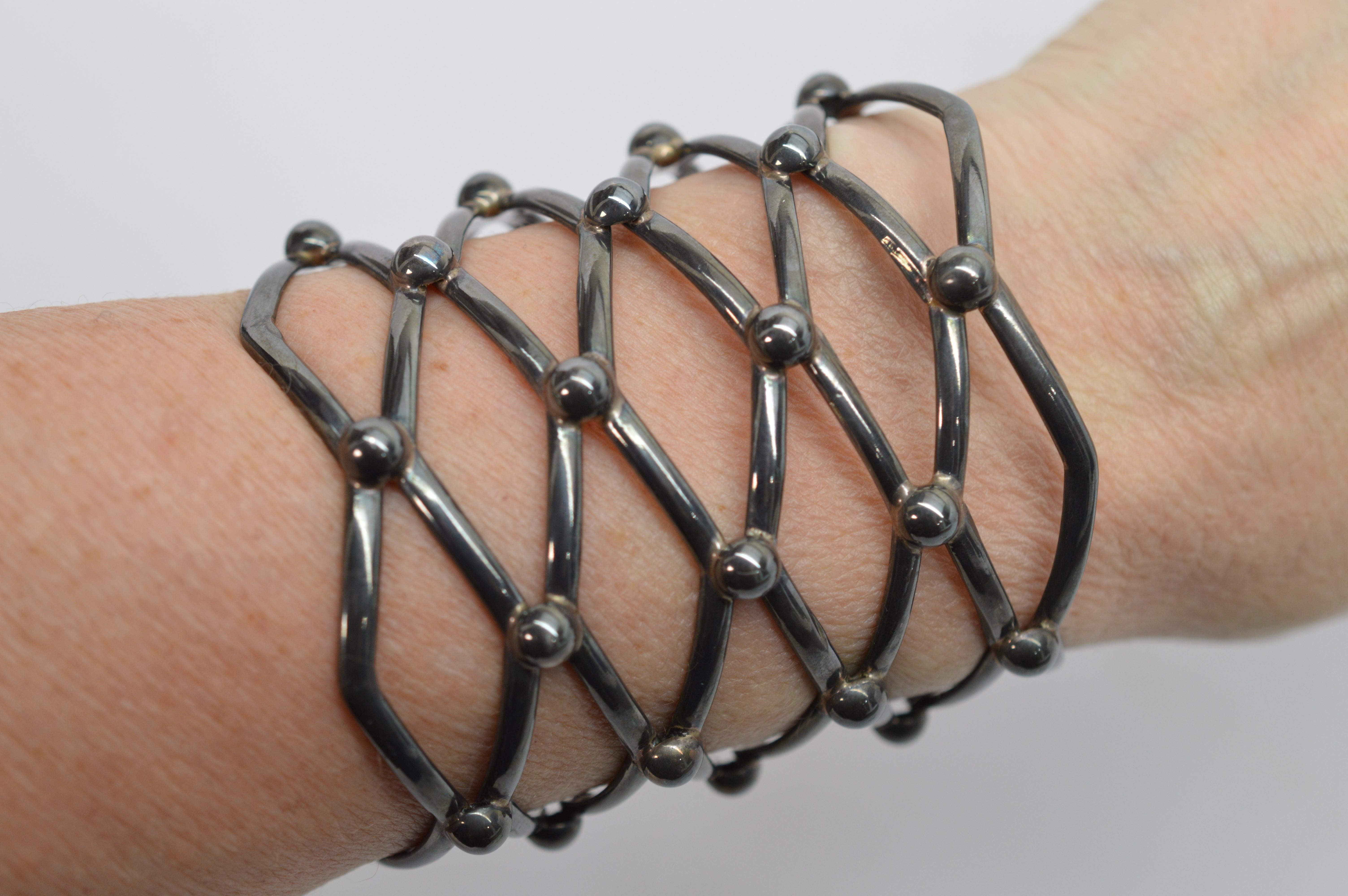 Questo bracciale in argento con trama a reticolo, grande e lungo come un arciere, è un'audace dichiarazione di stile. Creato artigianalmente, questo pezzo misura 2-7/8 pollici di lunghezza e 2-3/8 di larghezza, con una circonferenza di circa 6-3/4