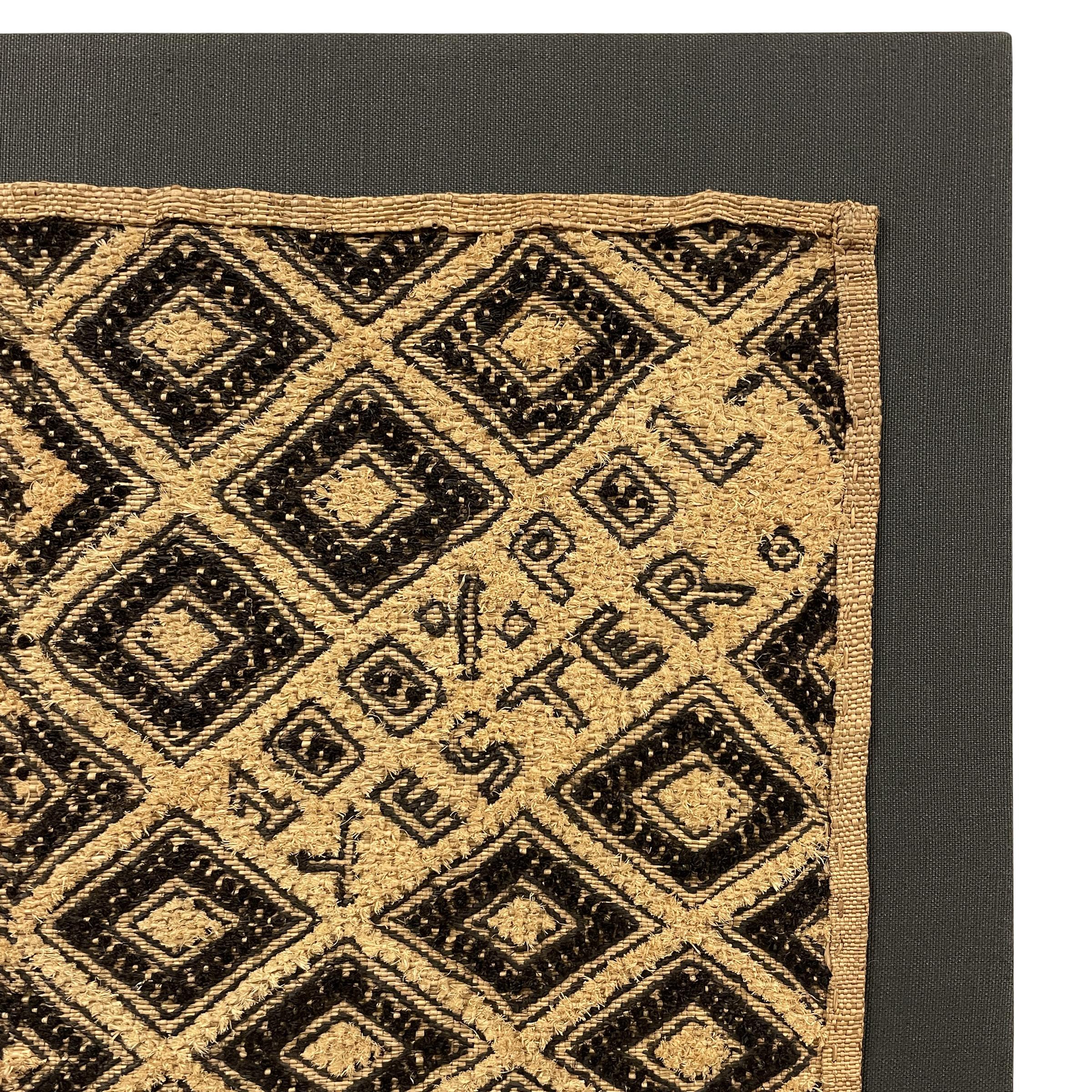 A provocative late 20th century Kuba cloth panel with a bold zigzag and diamond pattern woven in black and natural cut pile raffia surrounding a tongue-in-cheek inscription reading, 