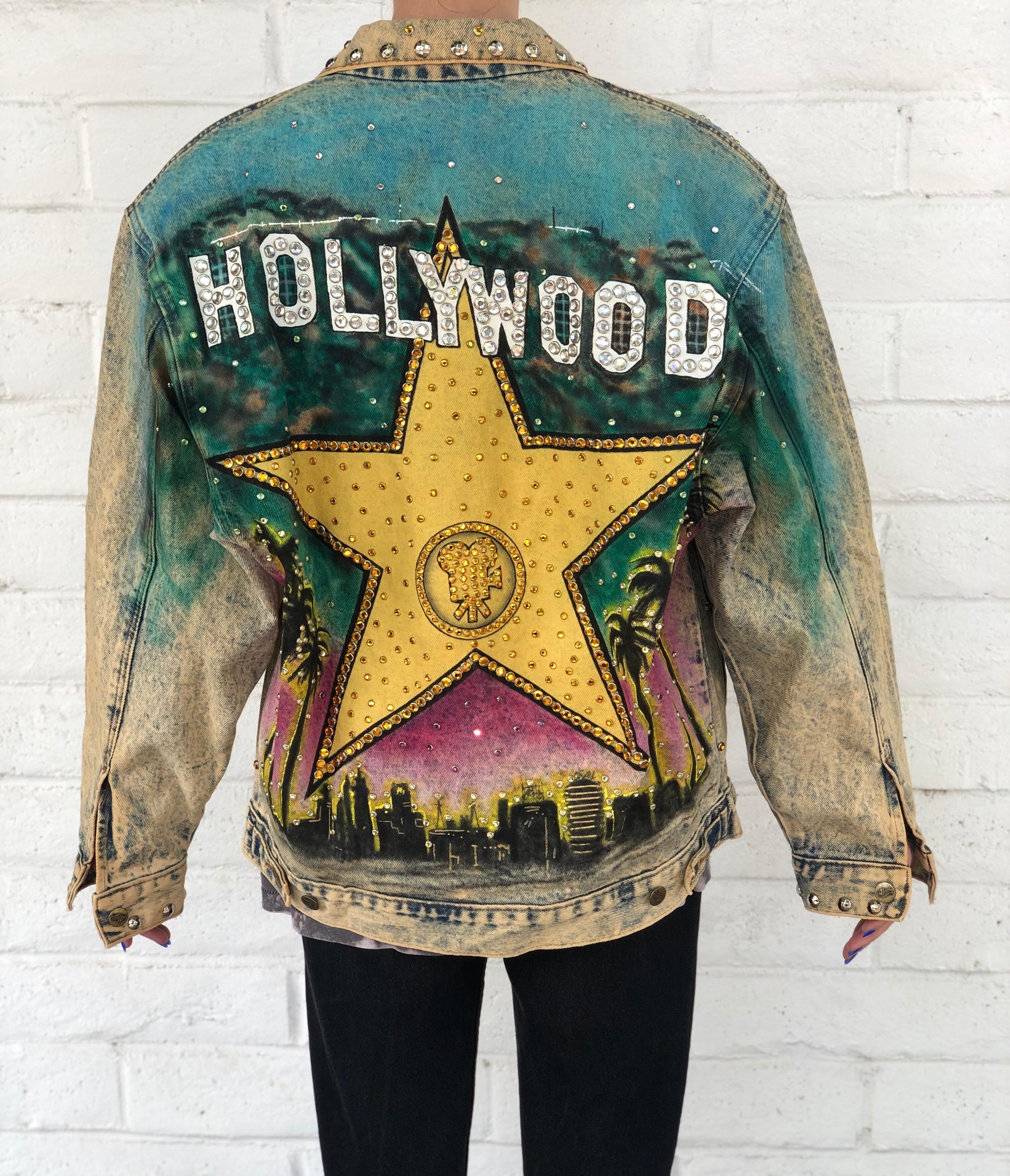 Feel like the ultimate Hollywood star with this Tony Alamo jean jacket! Circa 1987, this oversized jean jacket features an acid wash, brass toned buttons, two front pockets and eye-catching rhinestone embellishing throughout. The front of the jacket