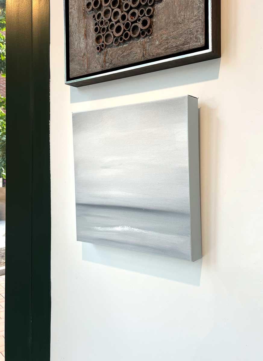This abstract painting by Tony Iadicicco features a light grey palette. The artist blends light shades of grey together to create an abstracted landscape composition, with a darker shade of grey running horizontally for an almost coastal scene. This