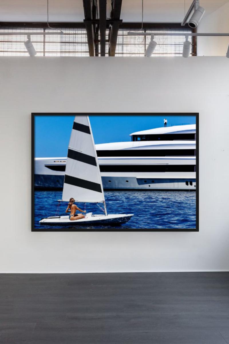 Eine Frau sitzt auf einem kleinen Segelboot und blickt auf eine Megayacht, die von Tony Kelly fotografiert wurde.

Alle Drucke sind in limitierter Auflage erhältlich. Erhältlich in mehreren Größen. Hochwertige Einrahmung auf Anfrage.

Alle Drucke