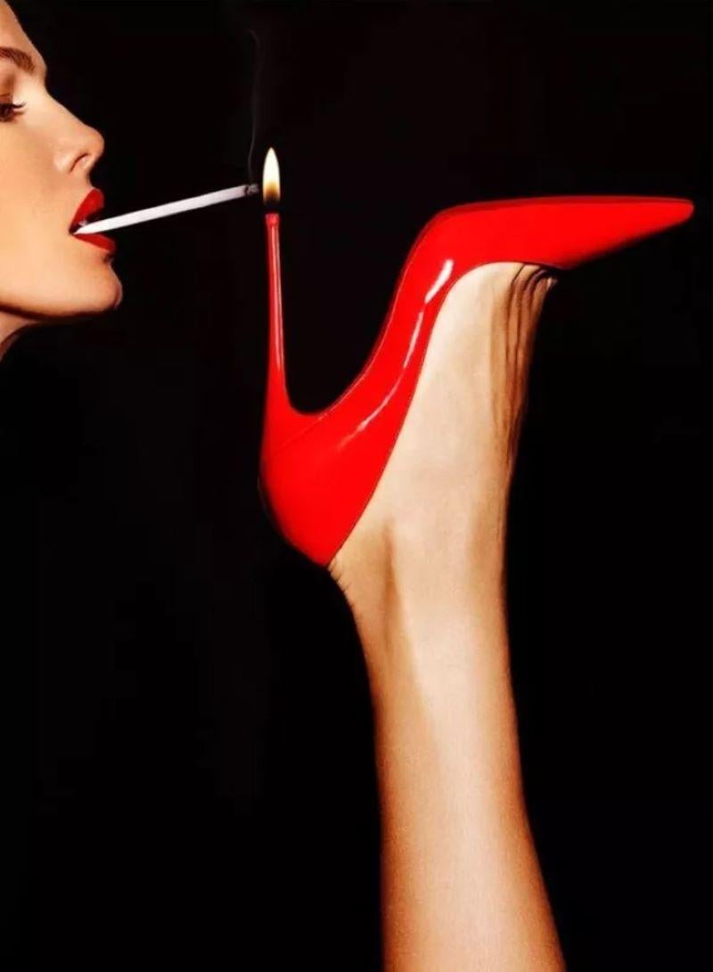 Tony Kelly Figurative Photograph – Super Slim - roter Schuh mit einer Frau, die ihre Zigarettenflasche beleuchtet, Kunstfotografie