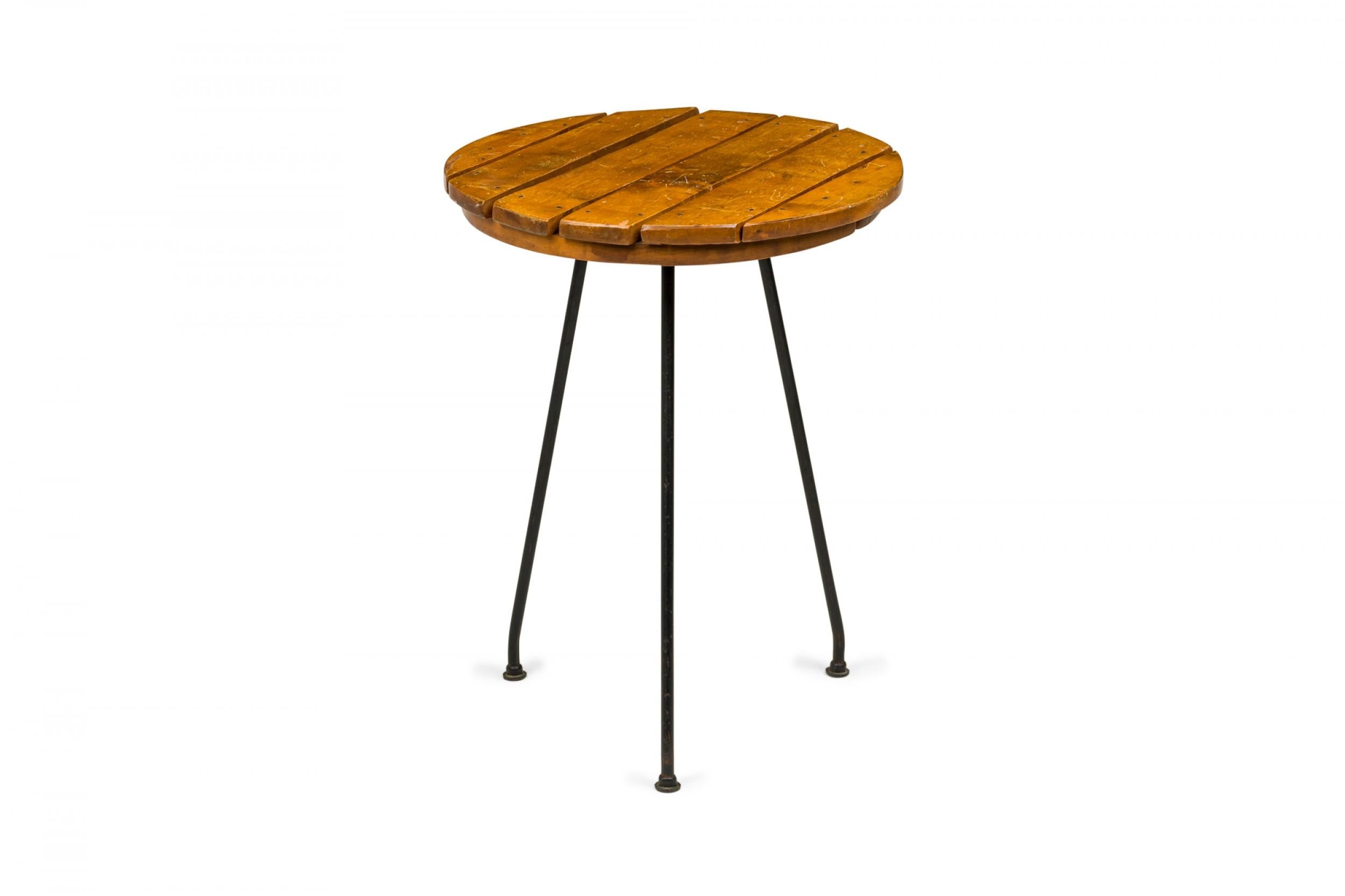 American mid-century circular end / side table with a wooden slat top resting on three angled black iron legs. (TONY PAUL)