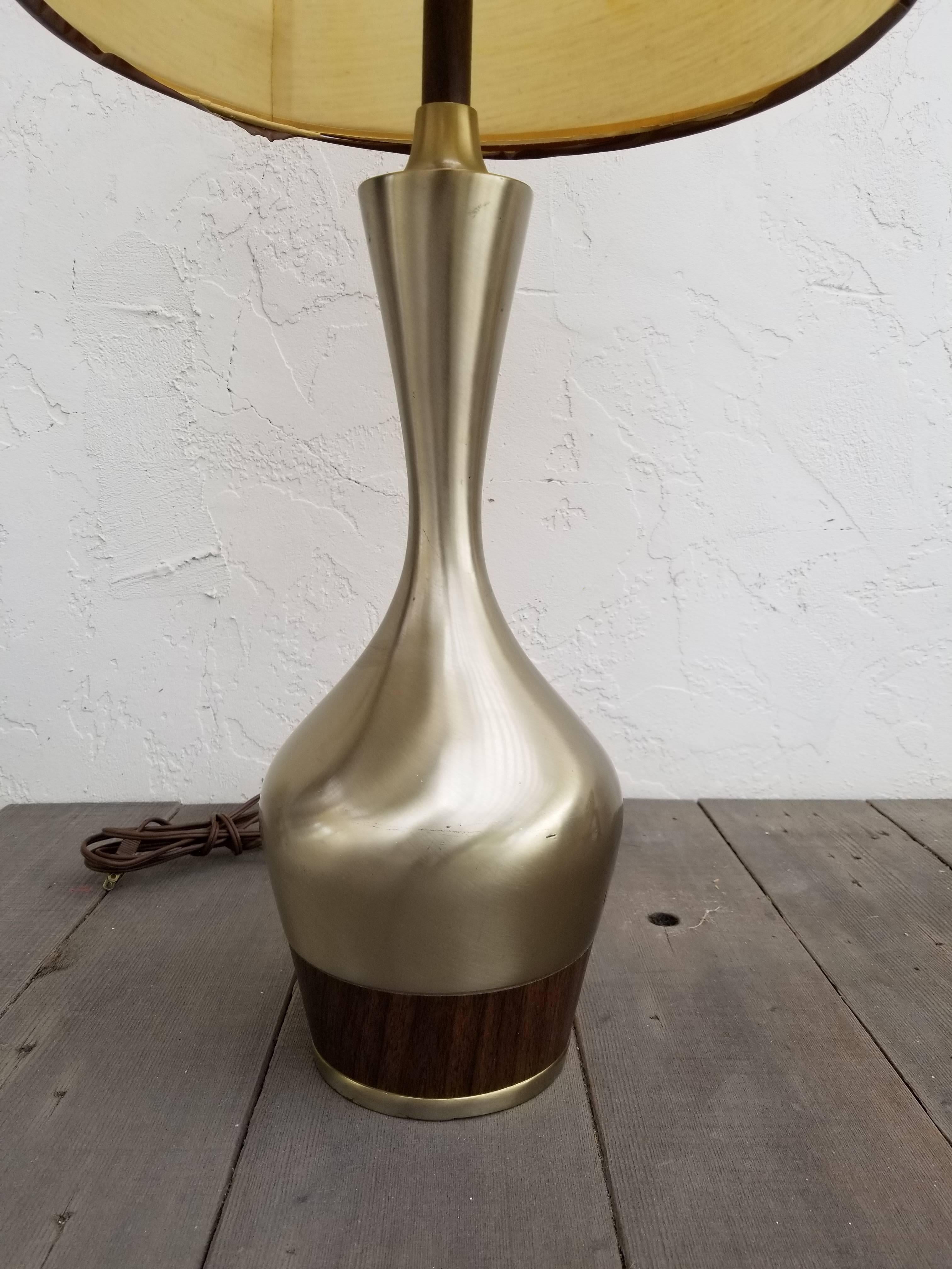 A Tony Paul design table lamp manufactured by Laurel Lamp Company, circa. 1960. Polished nickel finish and Amphora form creates interesting reflective quality. Contrasting hardwood band at base. Original laurel shade.