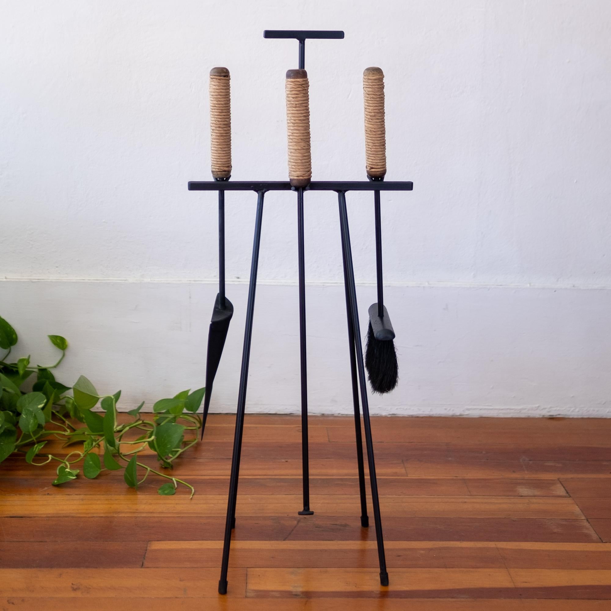 Iron and wood fireplace tools with cord-wrapped handles. Shovel, poker and broom on a floor stand. A striking functional and architectural design by Tony Paul, 1950s.