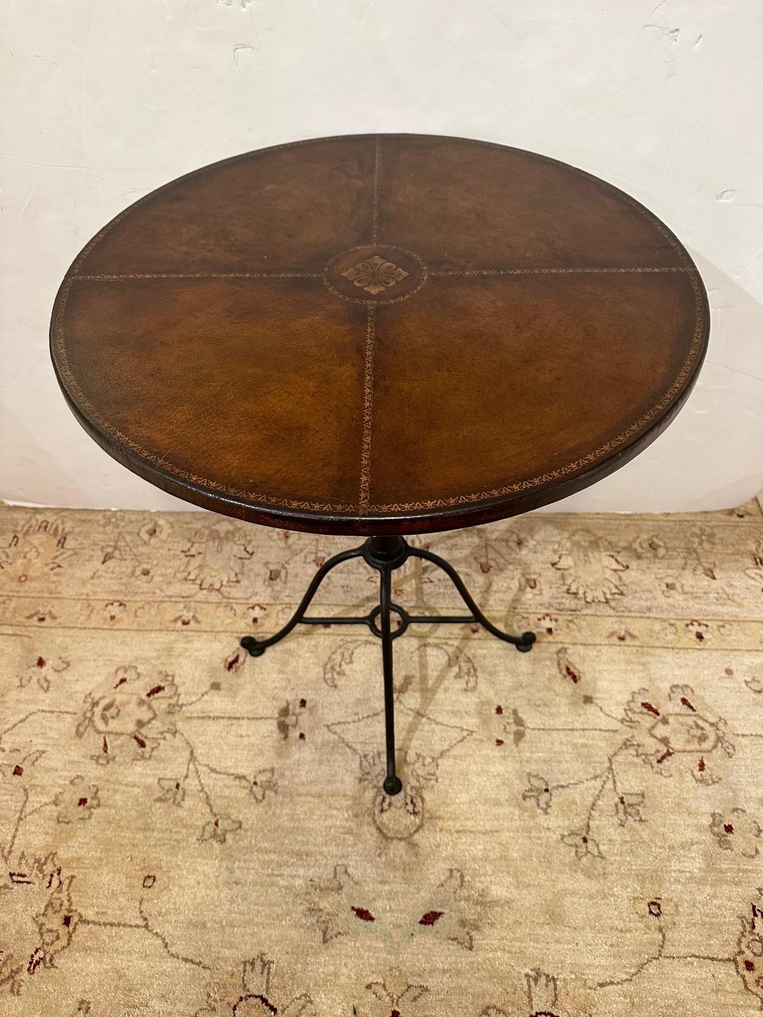 Great looking round side table or small bistro table having hand forged iron base and handsome brown tooled leather top with gold decorative embossing.
