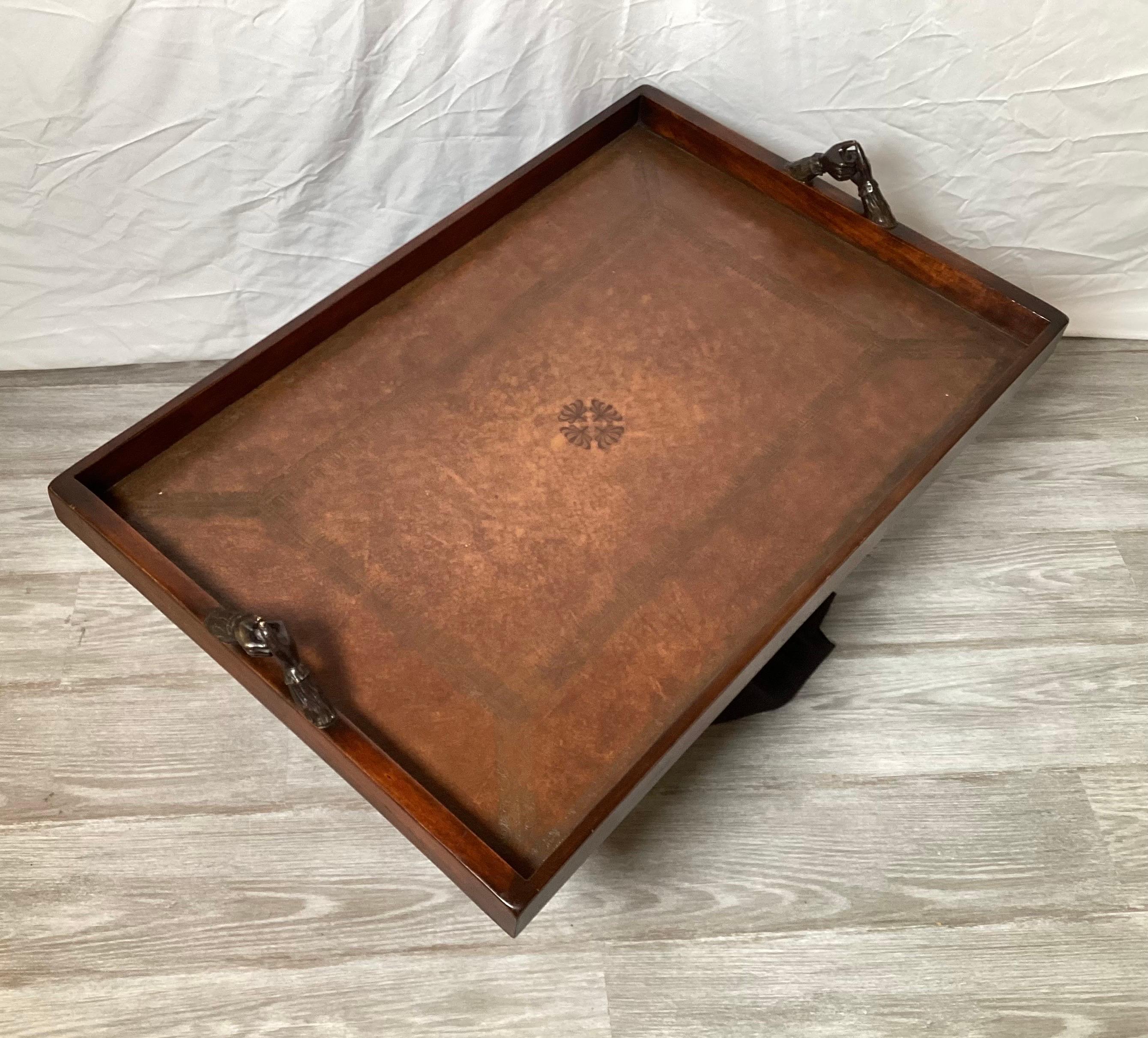 A leather covered drinks tray with cast bronze hands. The tooled leather over wood 32 inches long, 21 inches deep with a gallery edge all around.