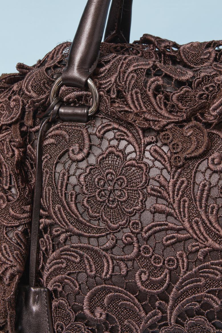 Borsa con manico superiore in guipure marrone su base in pelle. Chiusura a zip sulla parte superiore con tirazip del marchio. Chiave, portachiavi e armadietto. 2 tasche interne (una piccola con chiusura a zip e l'altra con chiusura a scatto) Fodera