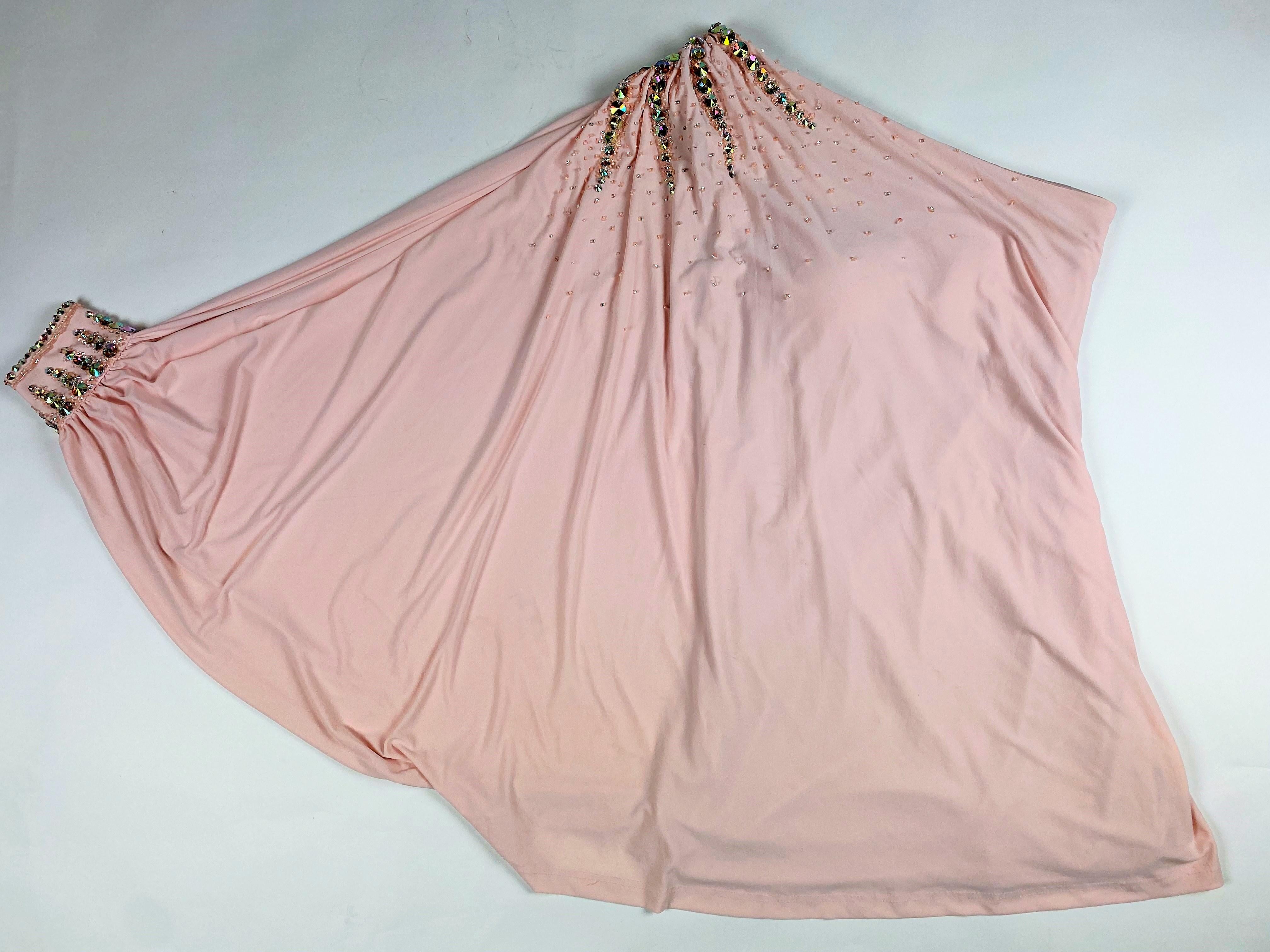 Early 1980s
France
Party or music hall top or mini-dress in powder pink stretch Lycra-Jersey, embroidered with glass beads and iridescent rhinestones. Large asymmetrical neckline with epaulettes and theatrical batwing sleeves, giving this top plenty