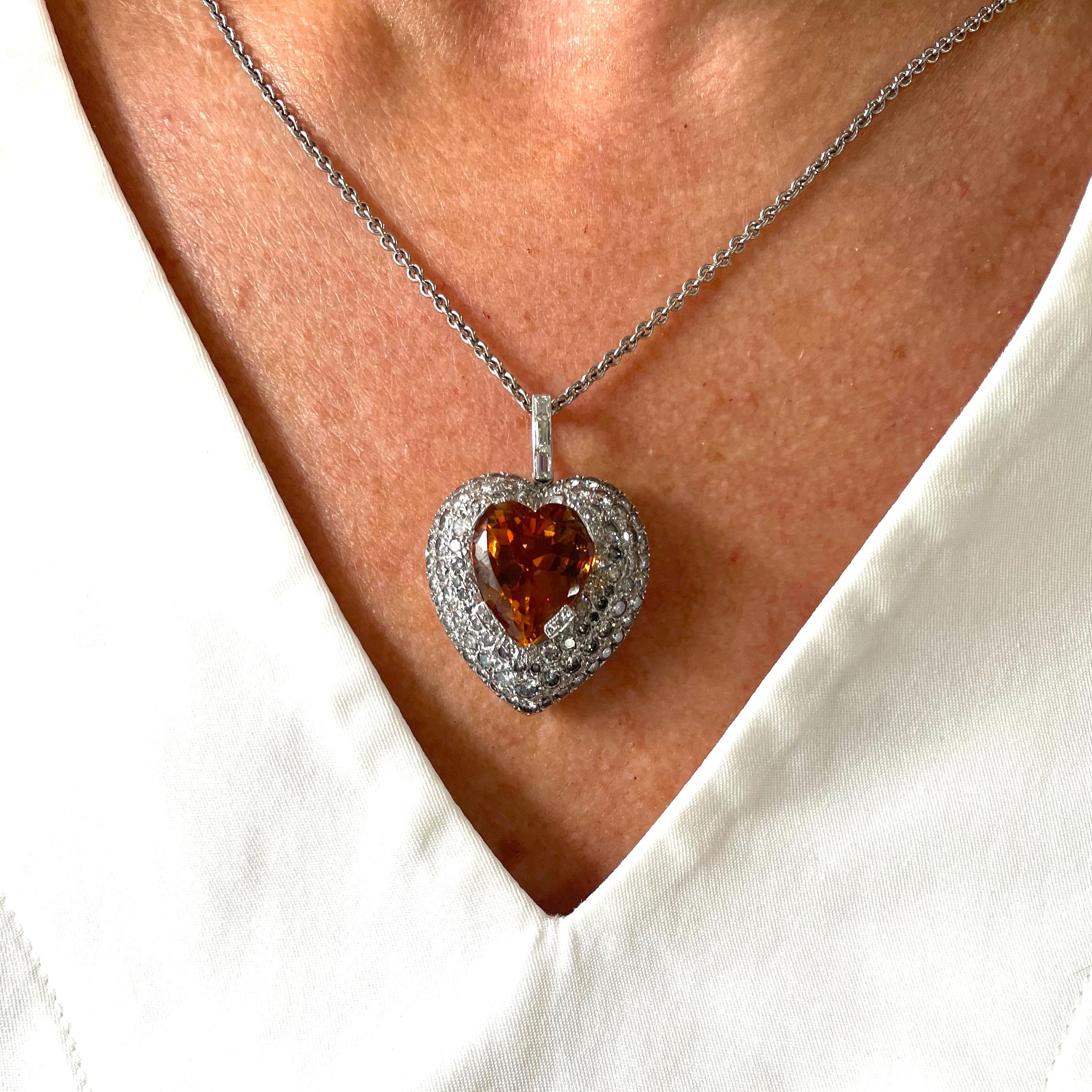 A topaz and diamond heart pendant, central heart shaped orange topaz weighing an estimated 9.00ct, with a three row border of round brilliant cut diamonds and three baguette cut diamonds set to the bail, in white gold. 

The estimated total diamond