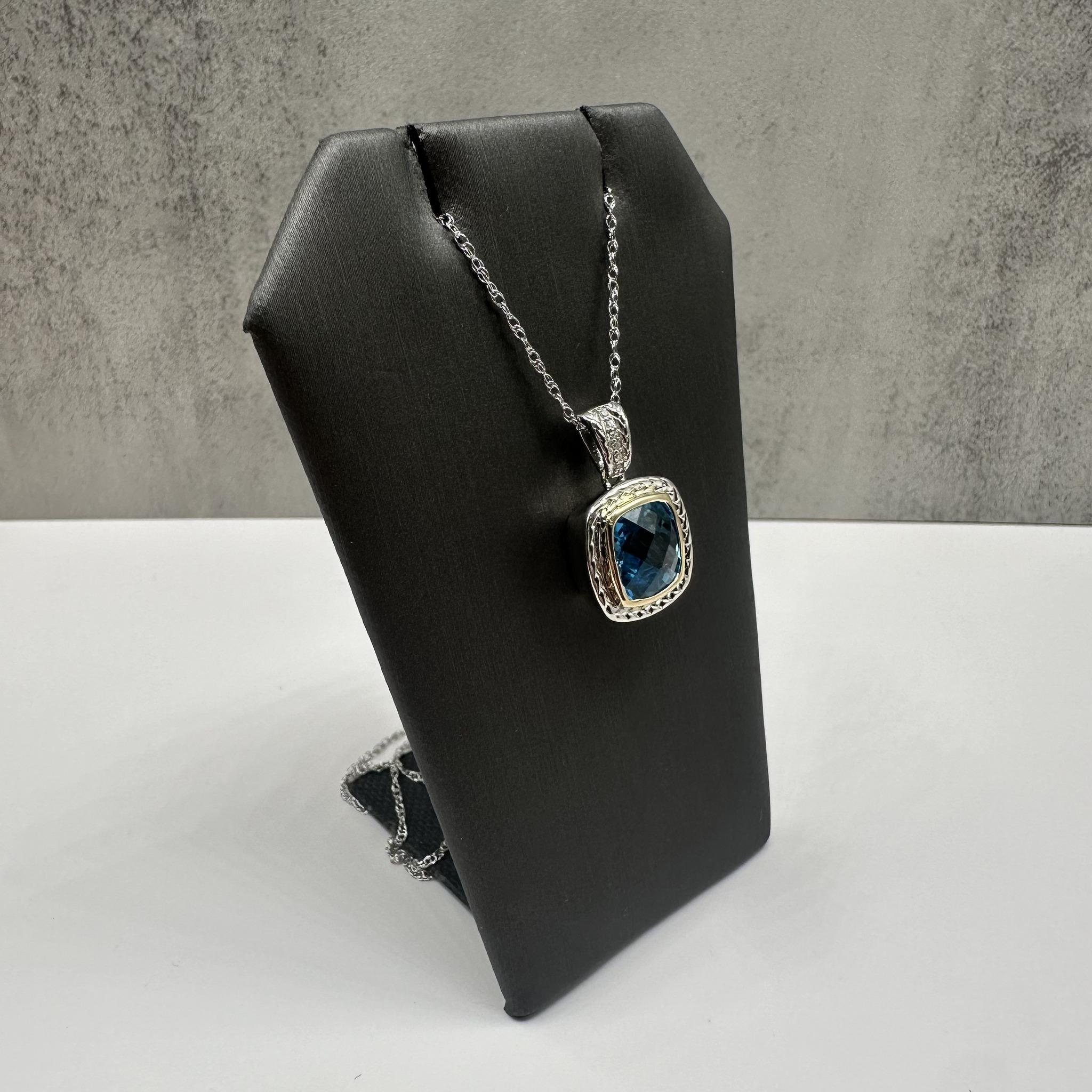 Questa elegante collana di topazi e diamanti in argento sterling con accenti in oro giallo 14 carati presenta un topazio blu di circa 10 mm con taglio a cuscino e 0,02 carati di diamanti naturali HI SI2-I1 a taglio singolo. Il castone che racchiude