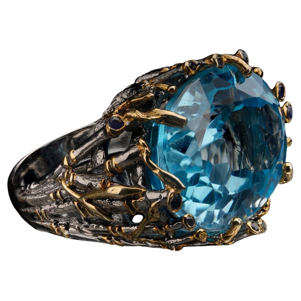 Cette topaze bleue massive, sans défaut et de taille ovale, remplit une monture unique en son genre, réalisée à la main, avec des pousses de bambou sculptées et des saphirs d'un bleu profond. Cette bague en argent sterling est ornée de feuilles